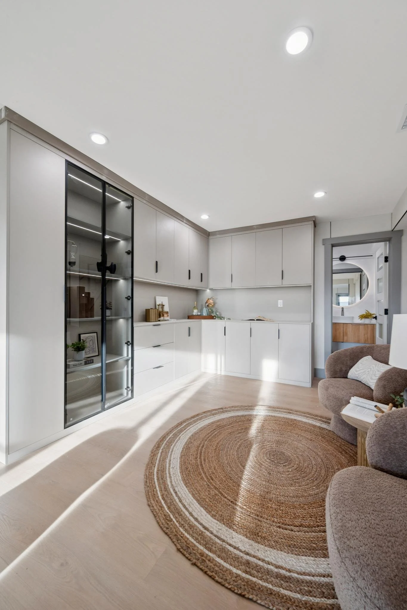 Modern living room with white built-in cabinets, a circular woven rug, a beige armchair, and a mirror in the background.