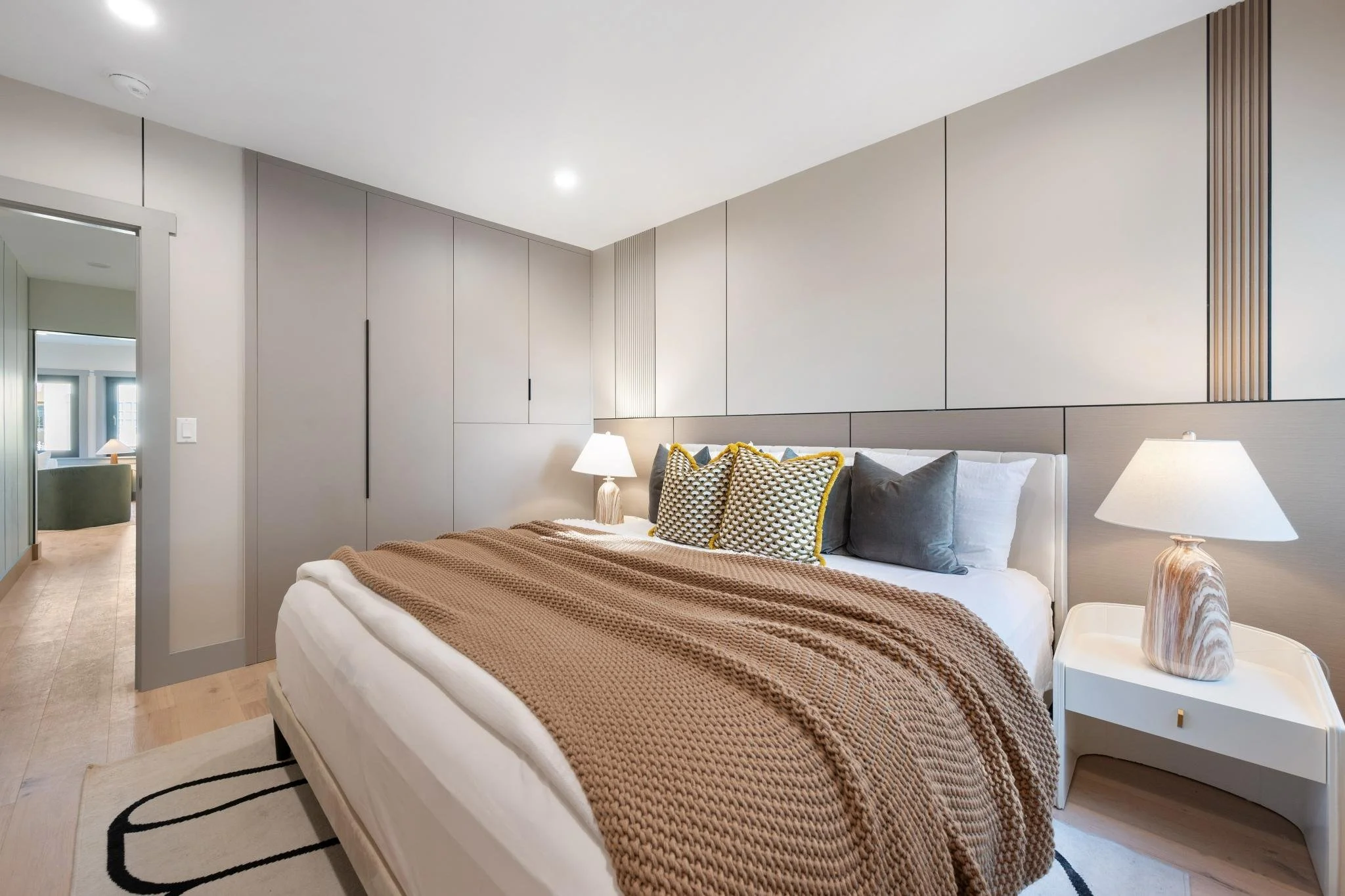 Modern bedroom with a bed, beige knitted blanket, decorative pillows, side table with marble-style lamp, and built-in closet doors
