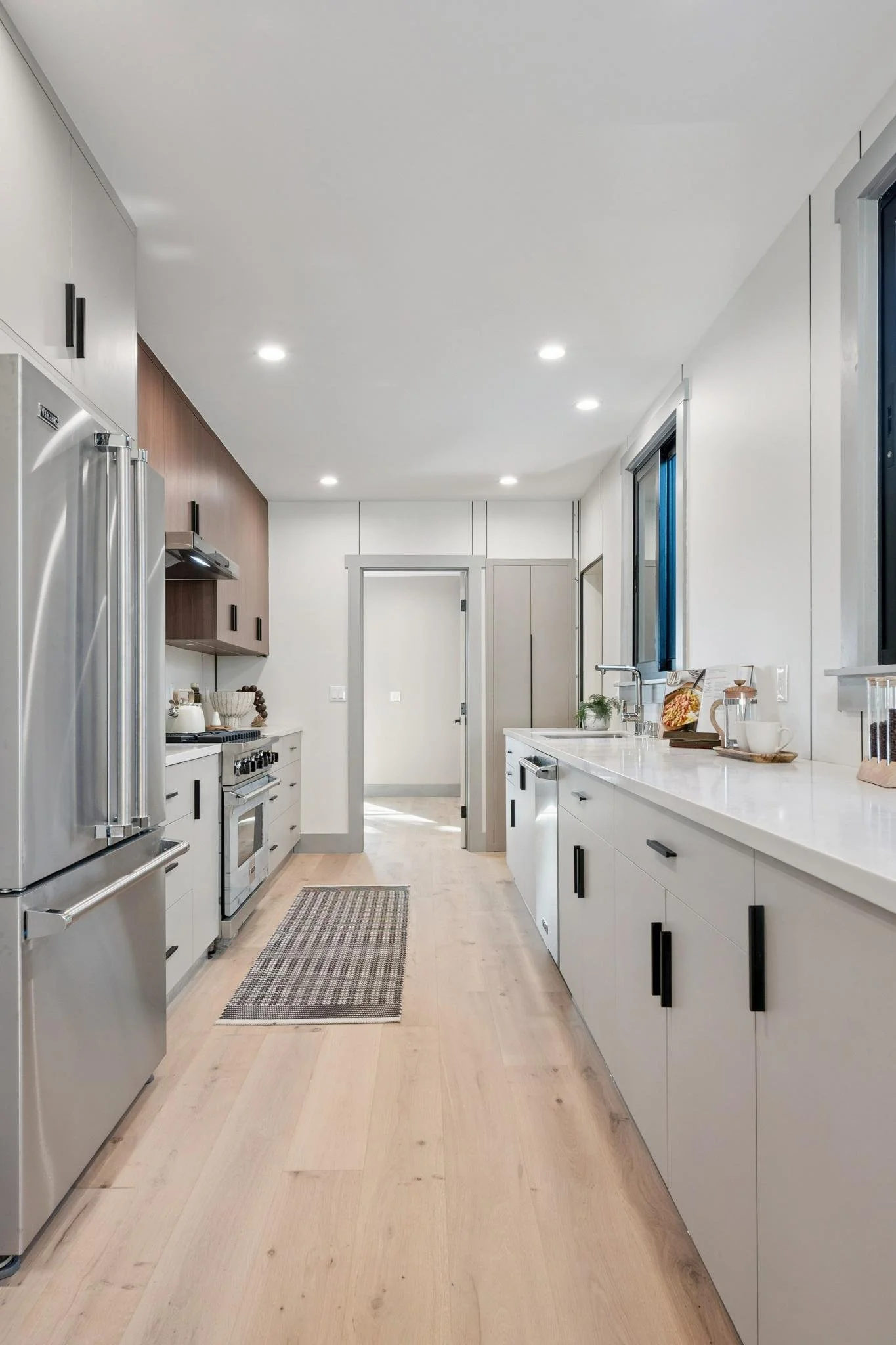 Modern kitchen with white cabinets, stainless steel appliances, black hardware, and light wood flooring.