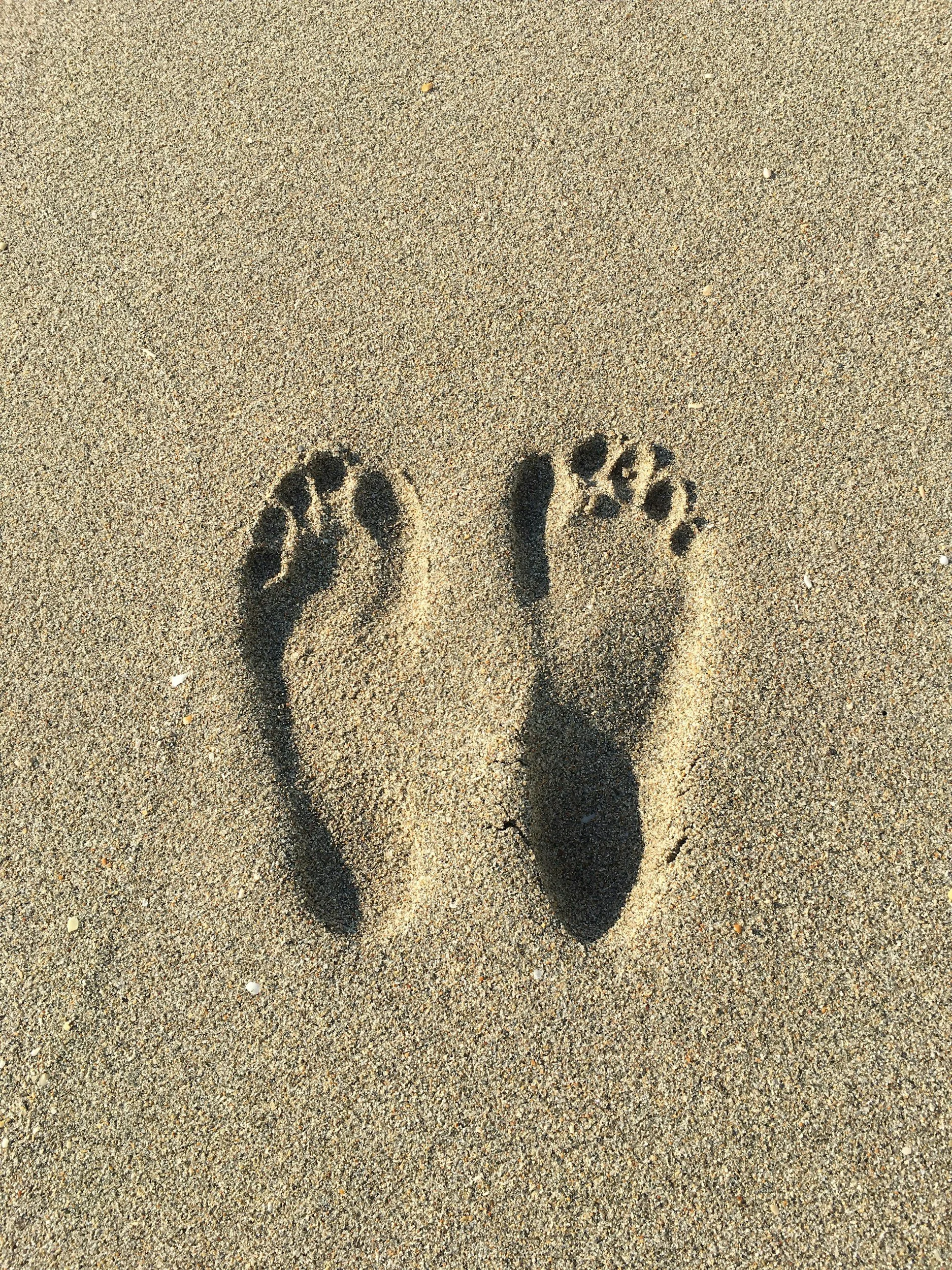 Shadow of two feet on sandy beach.