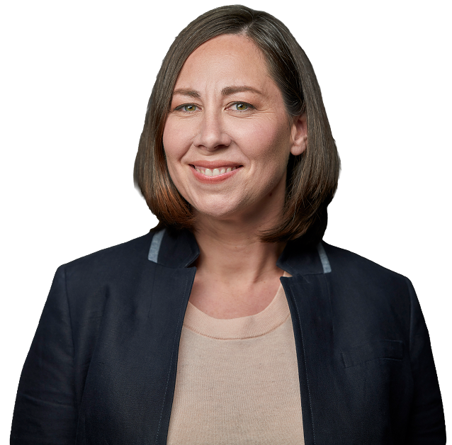 A woman with shoulder-length brown hair smiling, wearing a navy jacket over a beige shirt against a black background.