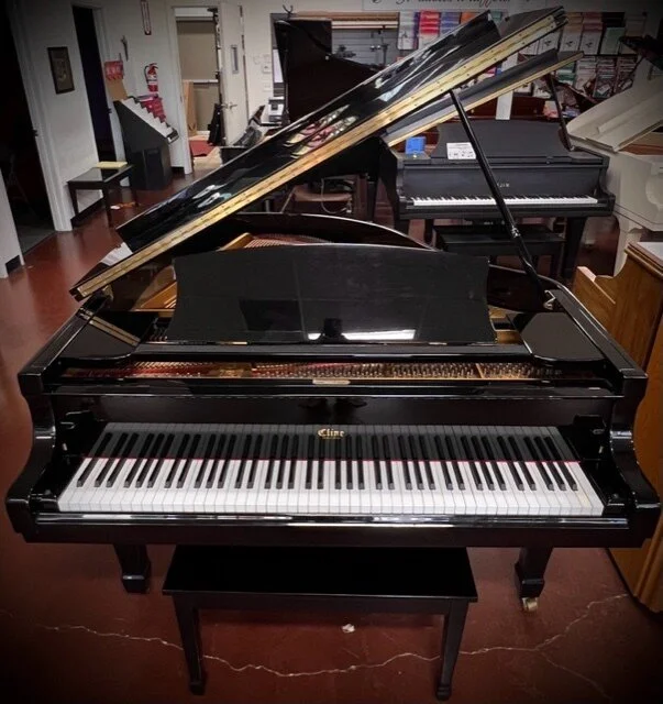 Black grand piano with an open lid in a music store or showroom.