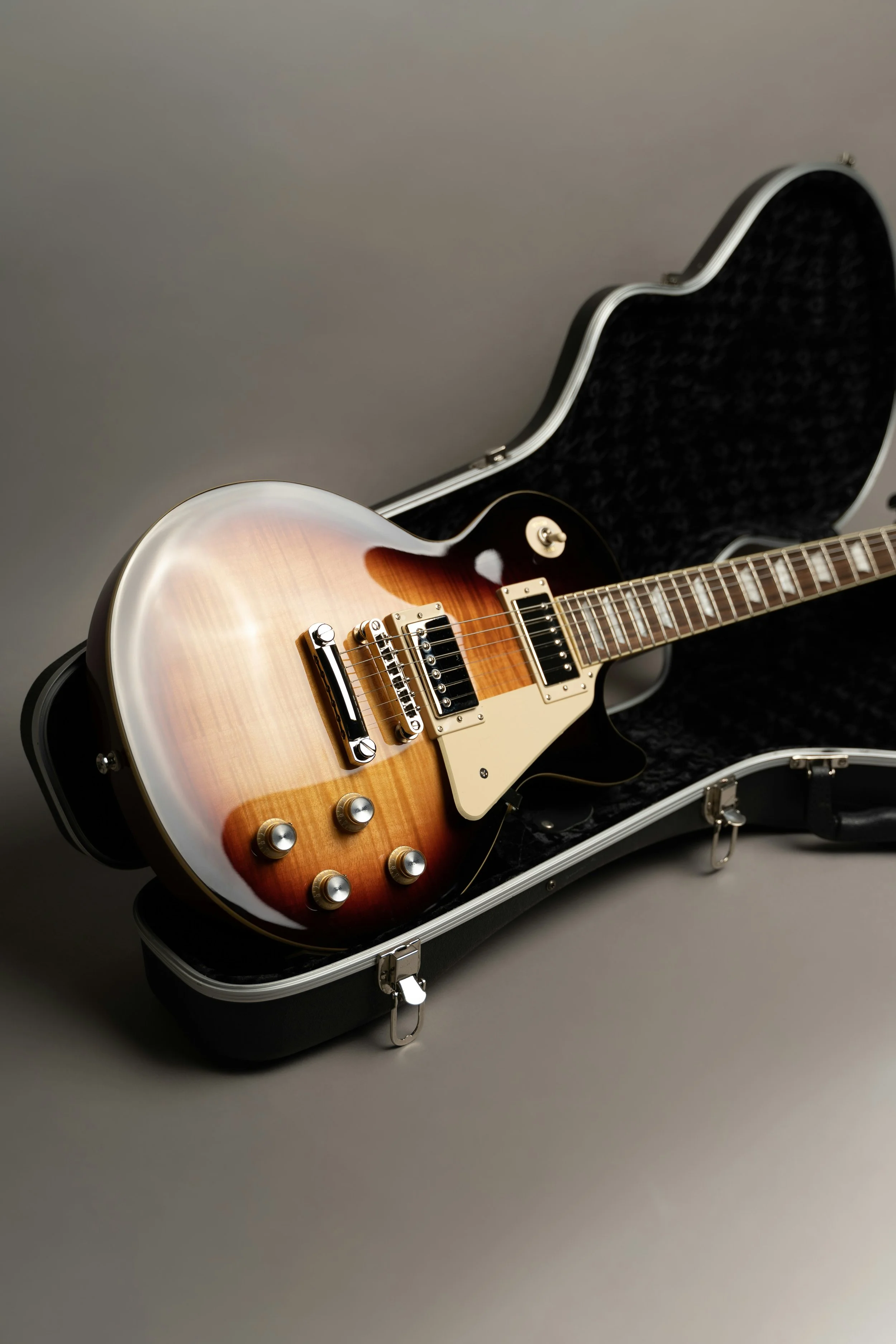 An electric guitar with a burst finish inside an open hard case with black interior plush lining on a plain gray surface.