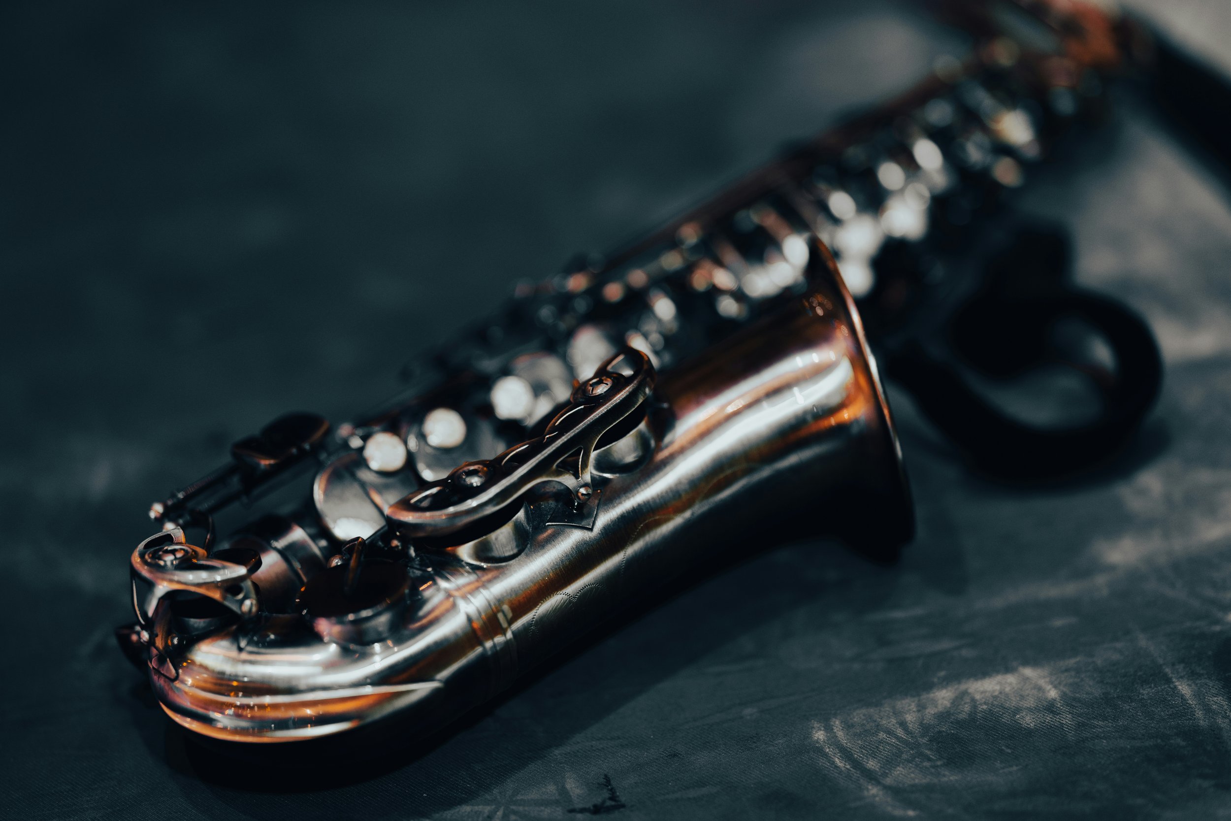 Close-up of a shiny, metallic saxophone with intricate keywork, resting on a dark surface.