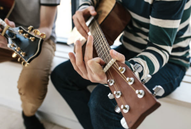 People sitting on a bench, playing guitars.