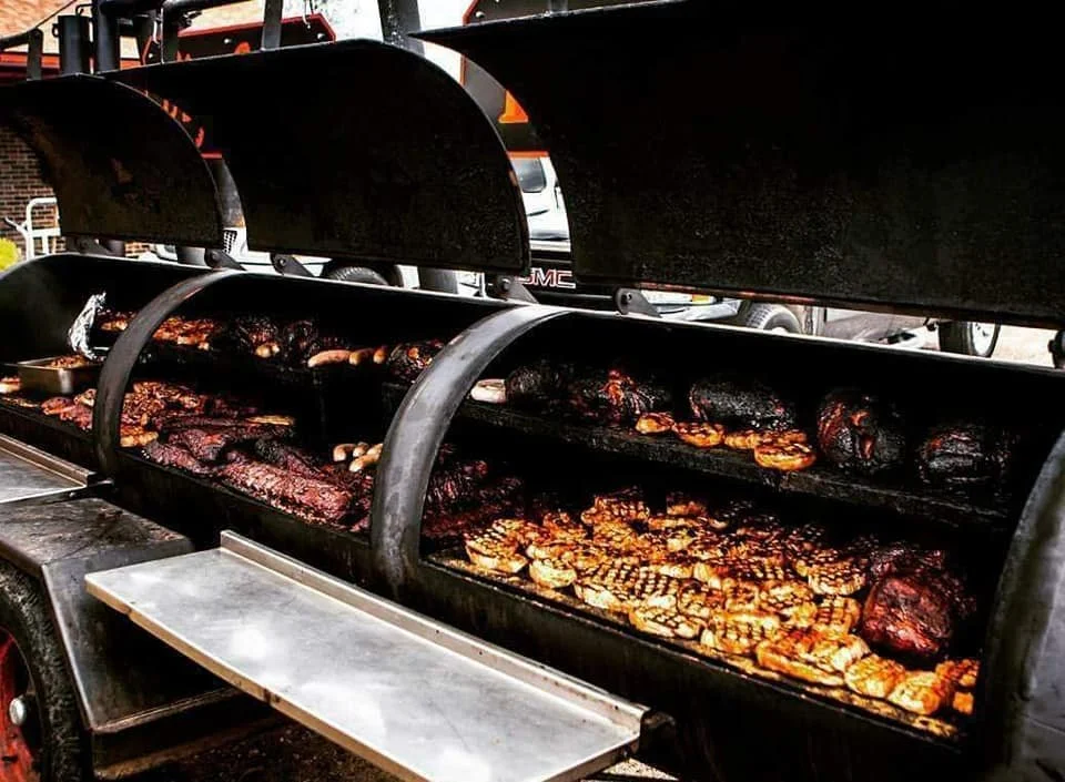 A large outdoor smoker filled with various meats including brisket, sausages, and ribs.
