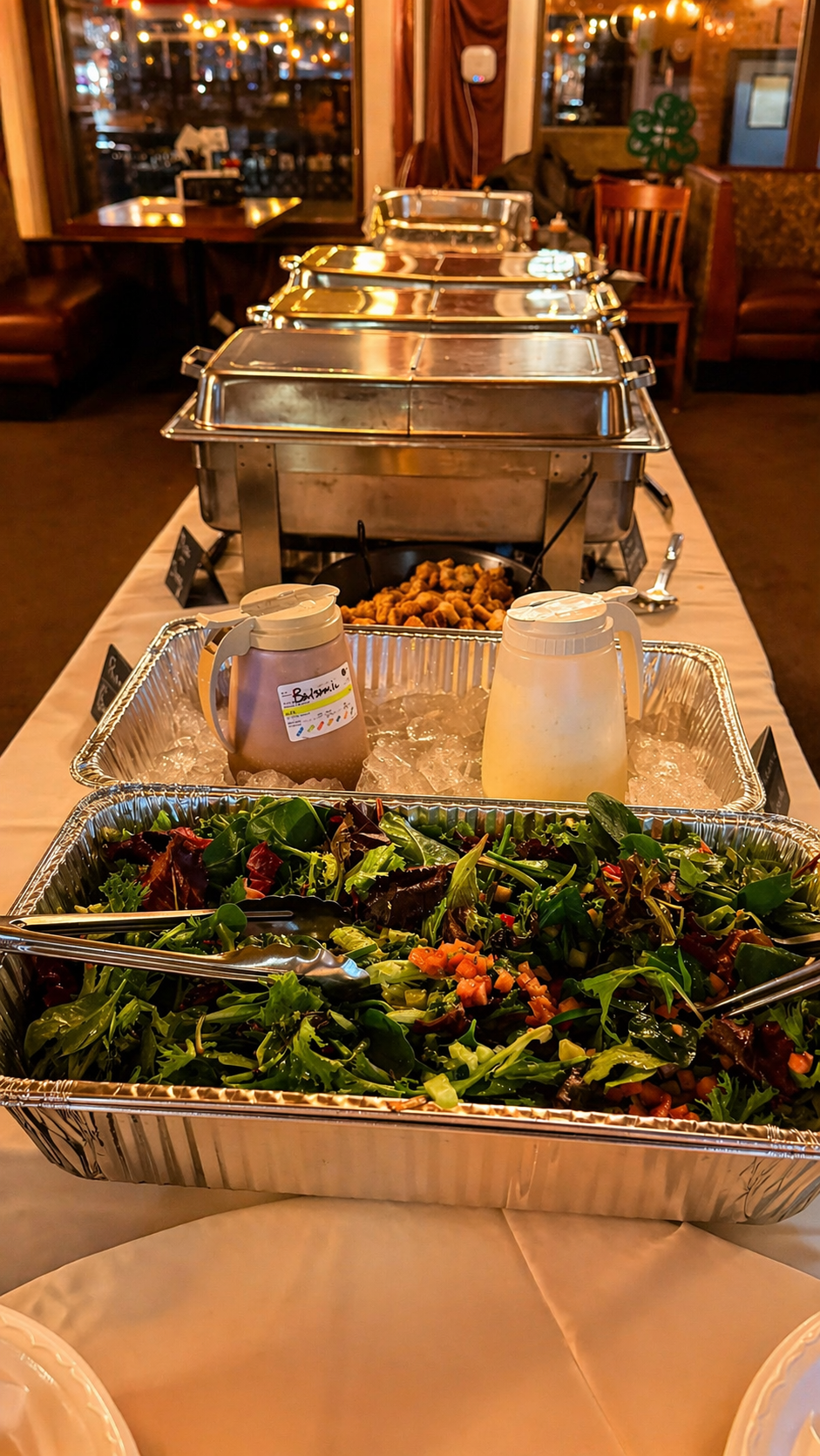 Buffet table with salads, dipping sauces, and warm dishes in a restaurant setting with warm lighting and wooden furnishings.