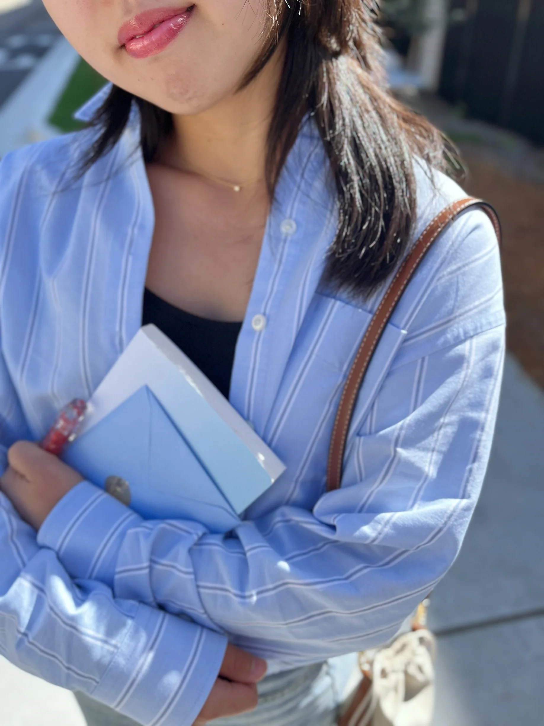 Woman in a light blue striped shirt holding a notebook, wearing a Chulip Conditioning Lip Gloss — product lifestyle shot