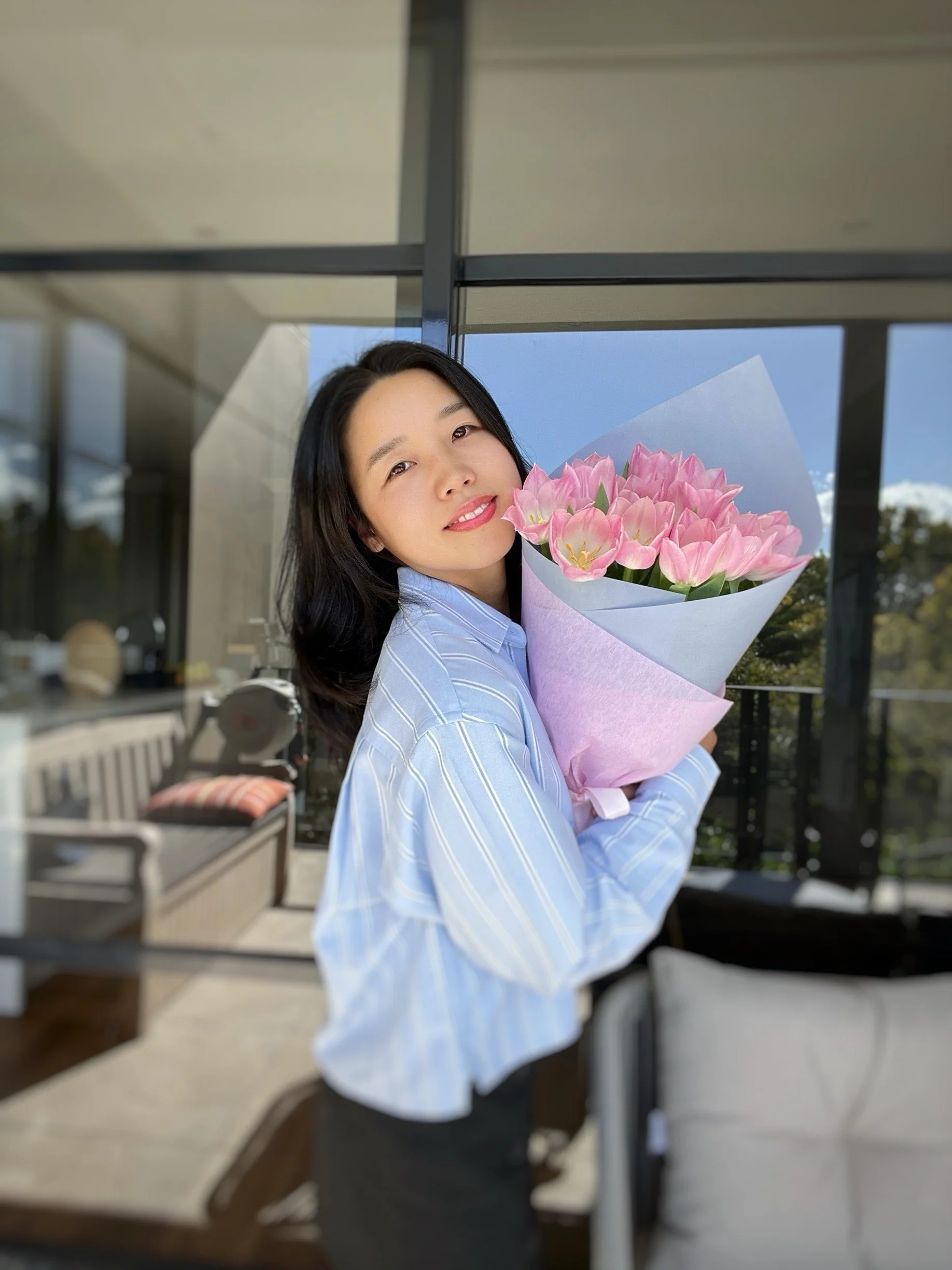 Chulip founder Yui smiling and holding a bouquet of pink tulips, wearing a light blue striped shirt — portrait photo of Chulip's founder