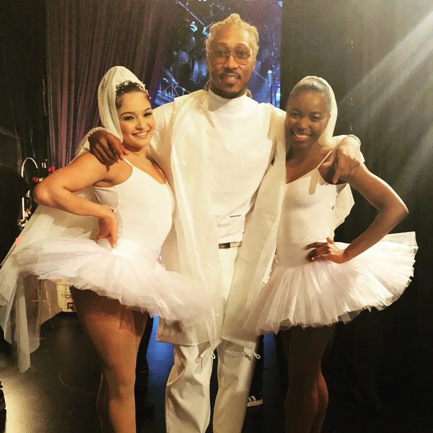 Three people, two women and one man, dressed in ballet costumes and standing together on stage.
