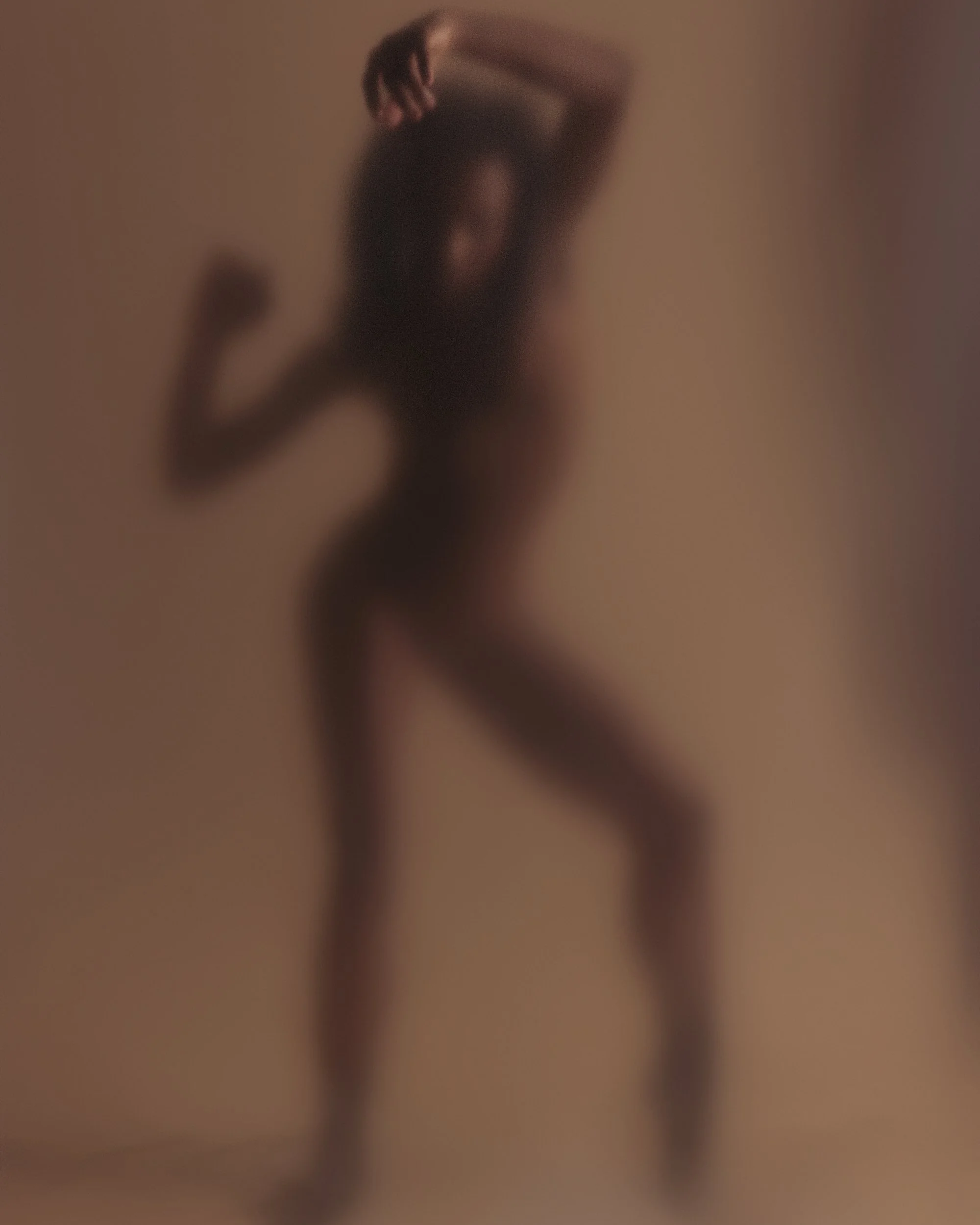 Blurred silhouette of a woman posing with one arm raised and one arm down against a plain background.