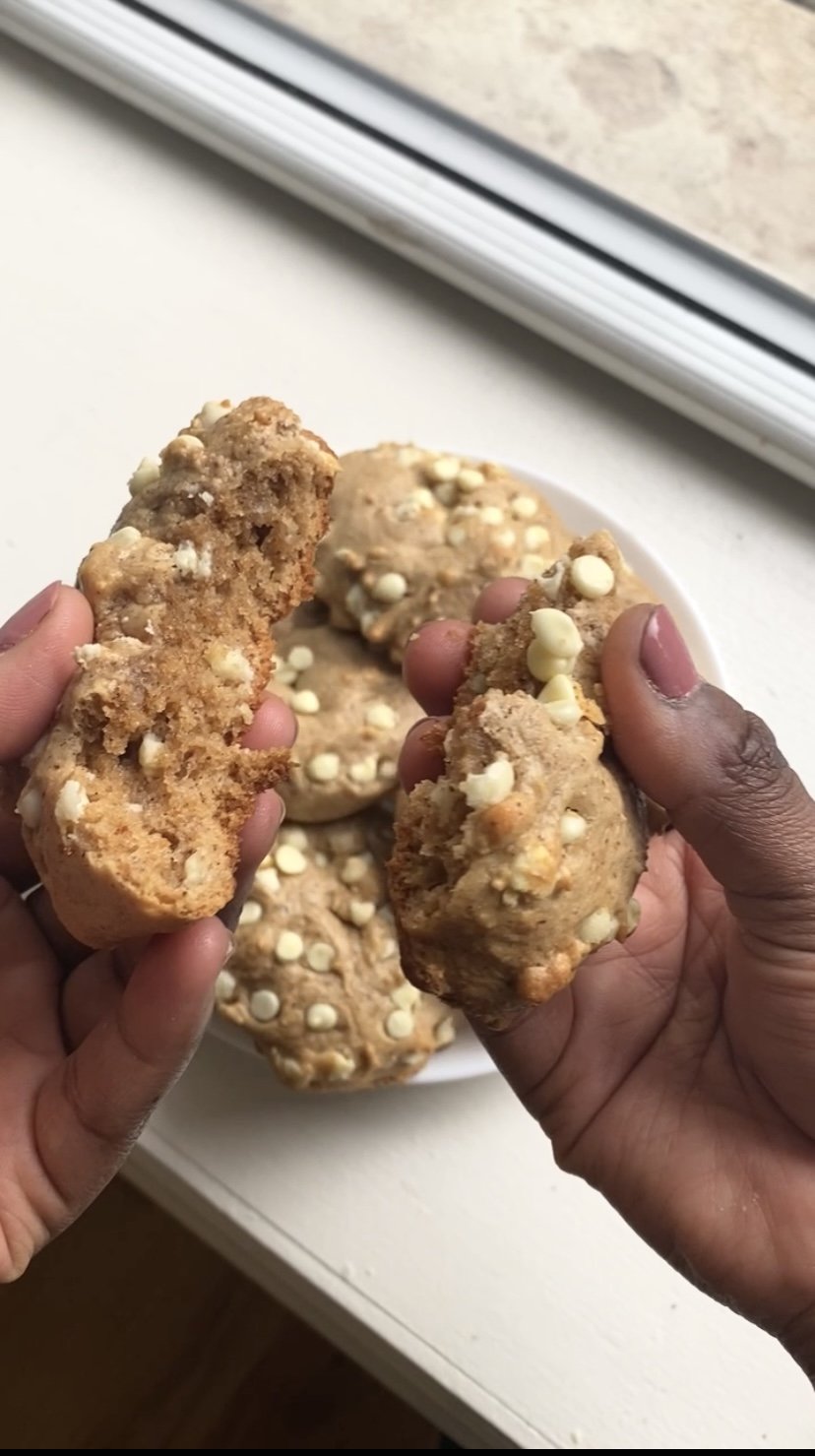 Two hands holding broken white chocolate chip cookies with a plate of whole cookies in the background.