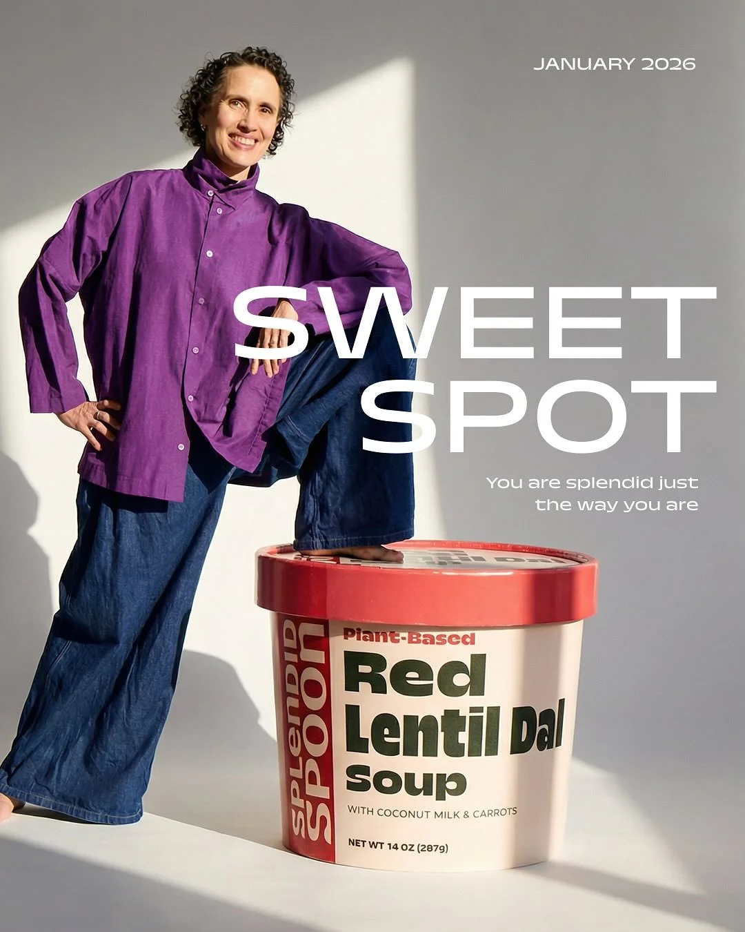 A woman in a purple shirt and blue jeans standing with one foot on a large container of plant-based Red Lentil Dal soup. The container has a red lid and white body with green and red text. The woman is smiling, with her hand on her hip and her knee on the container, against a plain background with a bright light and shadow. Text on the image reads 'SWEET SPOT', 'January 2026', and 'You are splendid just the way you are'.