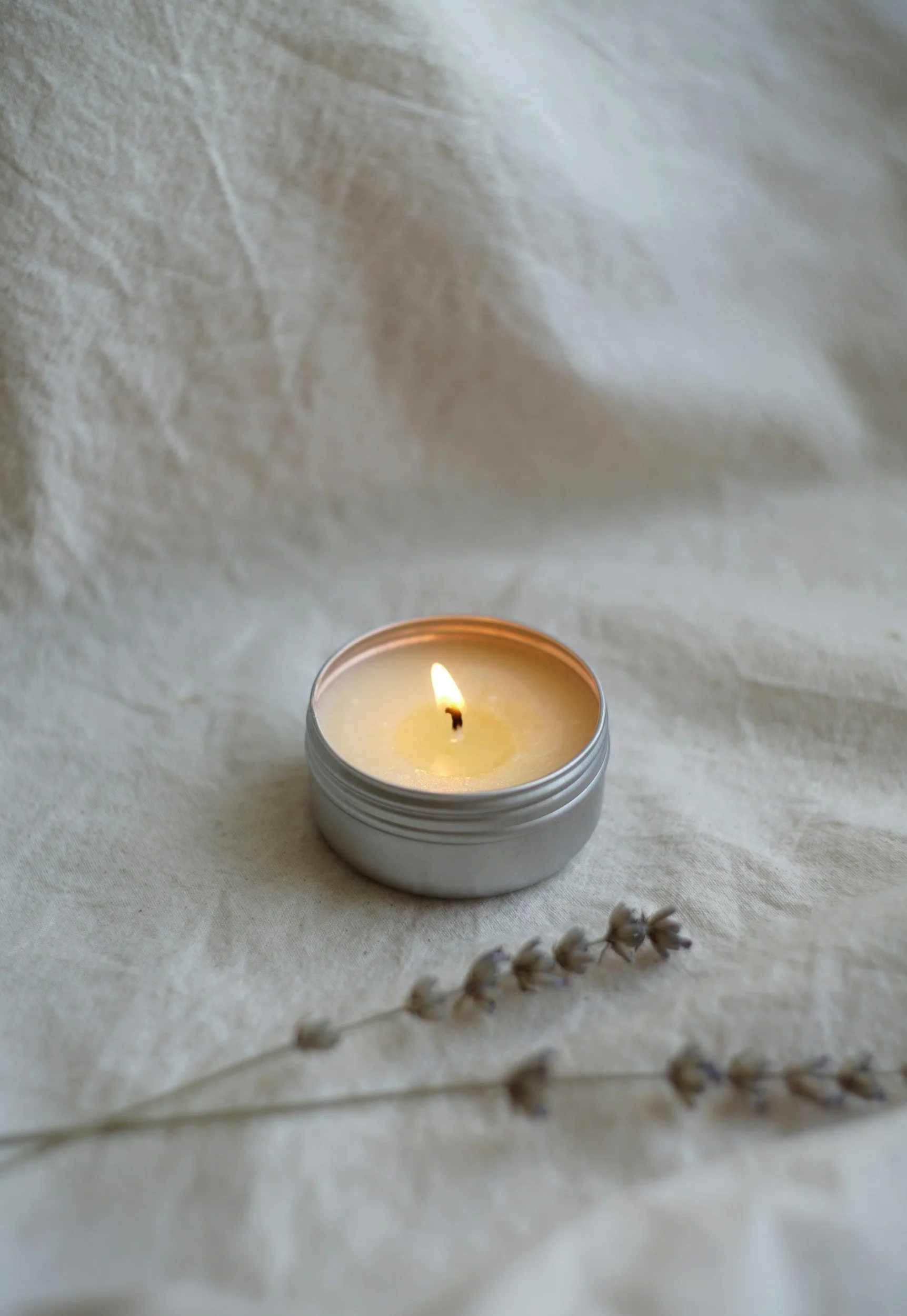 A lit white candle sits on an in-home massage table with white sheets.