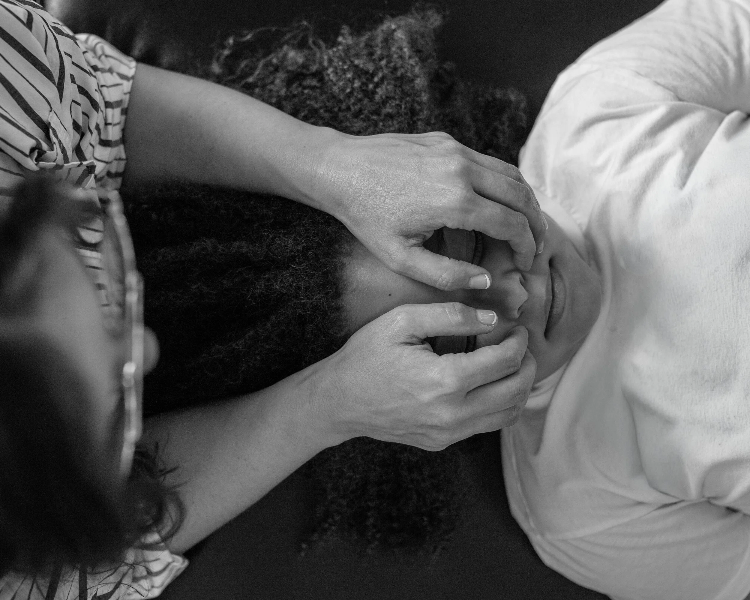 Close-up of two people holding hands, with one person's face partially visible and the other's face not visible. The scene is in black and white.