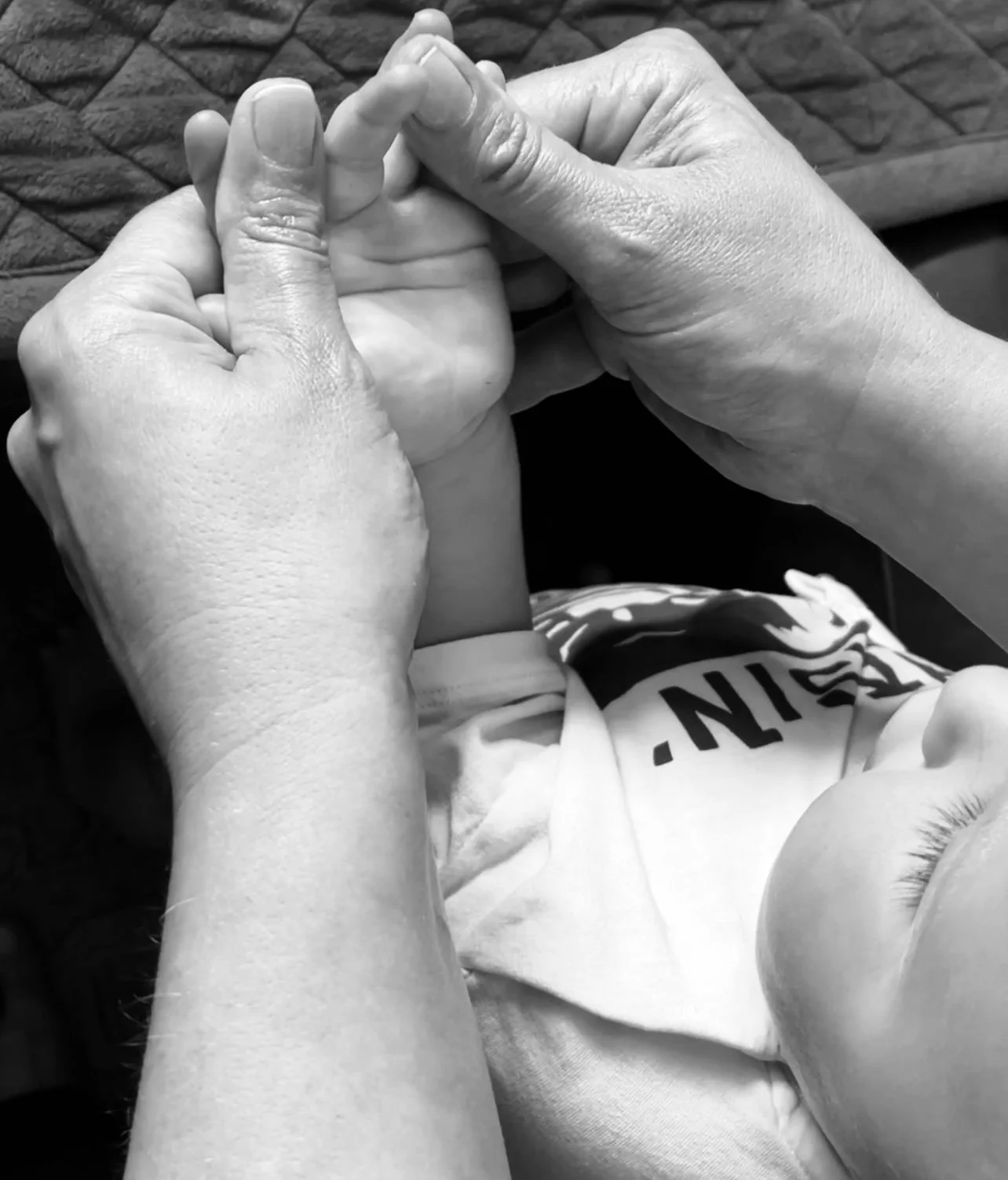 A black and white photo of a person's hands holding a baby's hand.