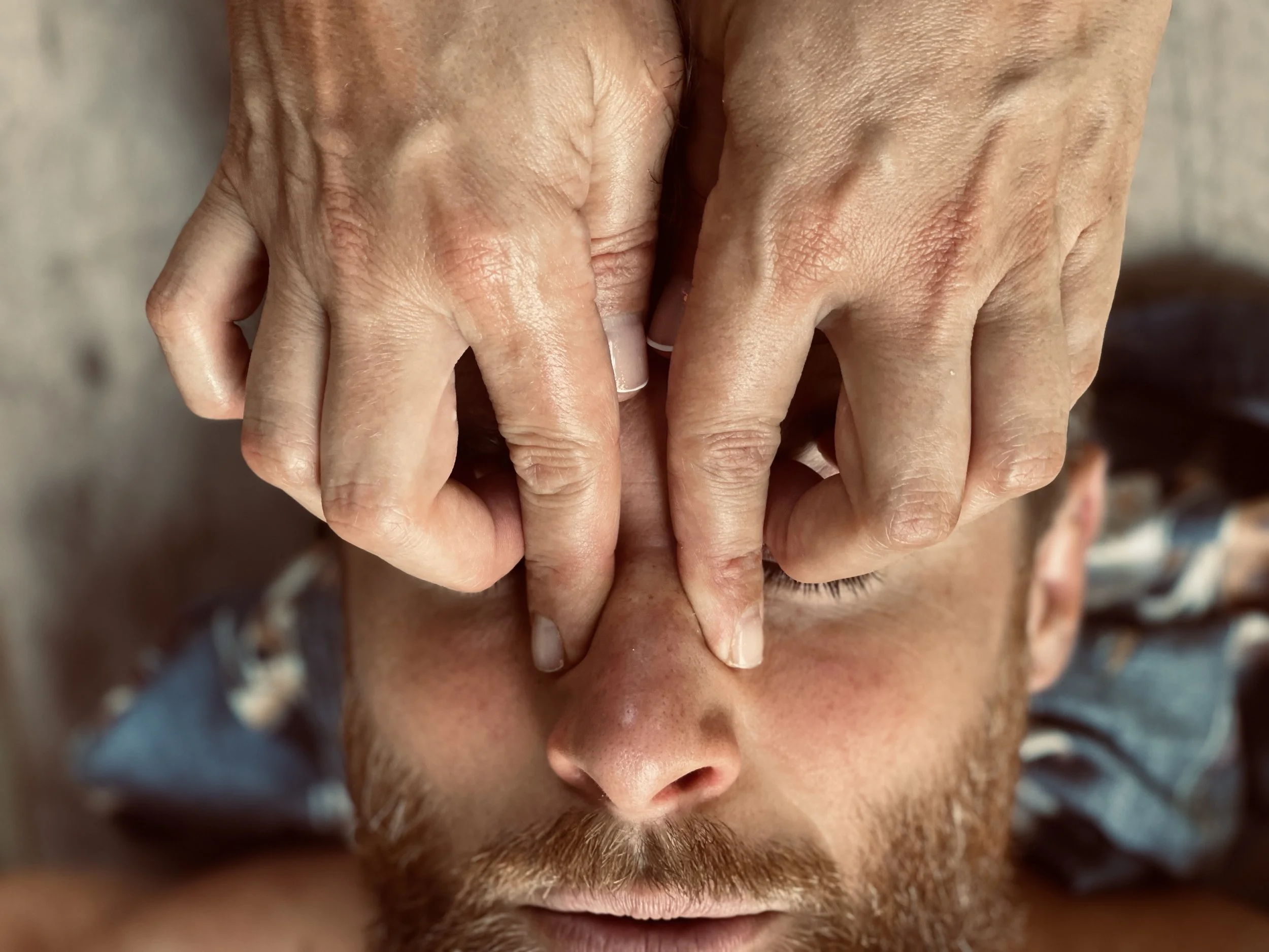 Close-up of a person with closed eyes receiving a facial massage or skincare treatment, hands gently pressing on their forehead.