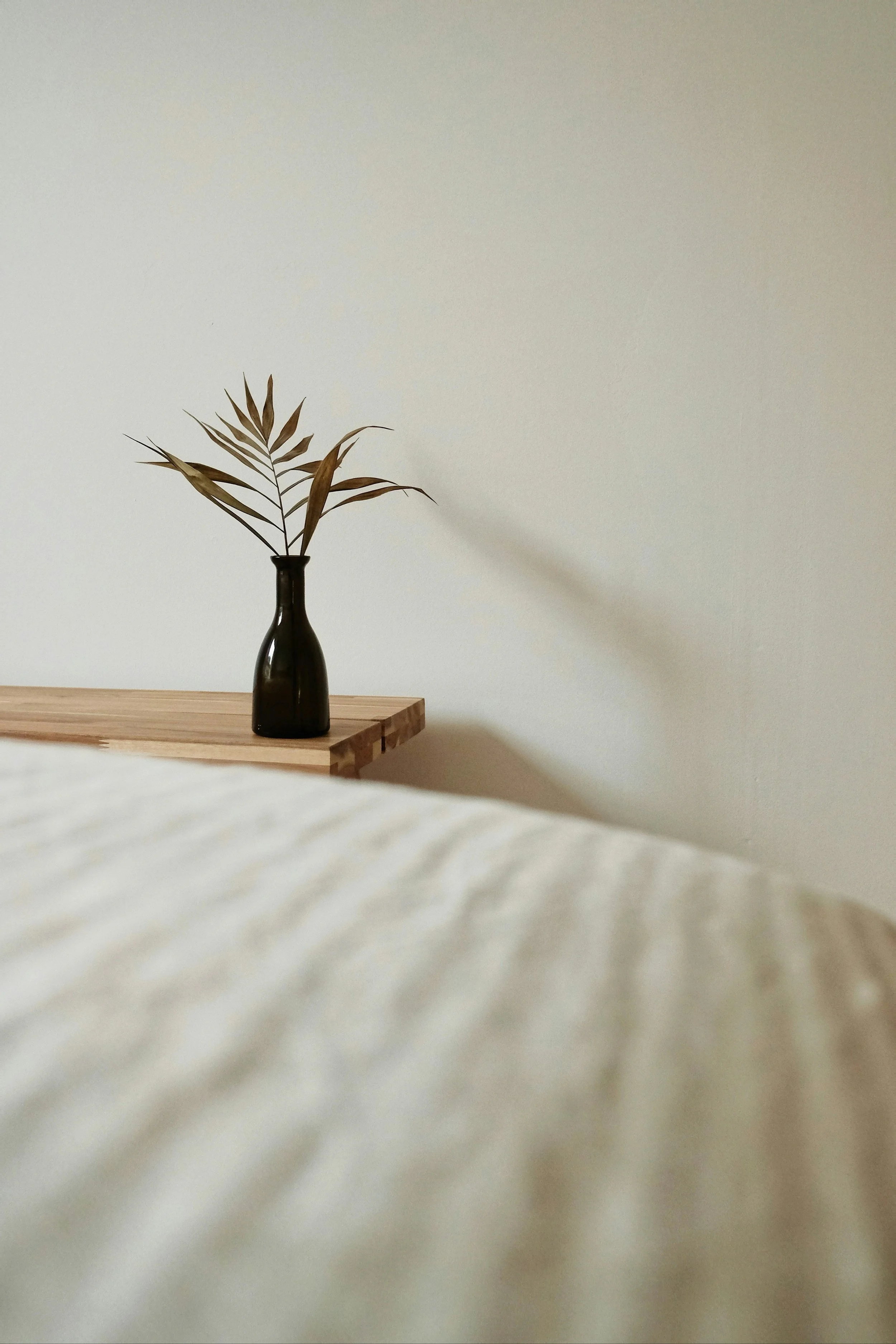 A black vase with dried leaves on a wooden table behind an in-home massage table.