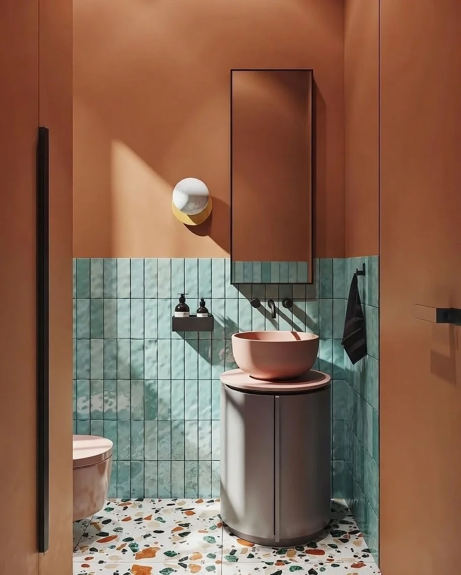 Modern bathroom with pink sink and matching toilet, teal tiled half-wall, orange walls, terrazzo floor, black towel rack with black towel, mirror cabinet, circular wall light.