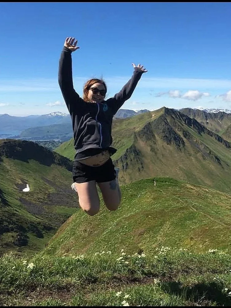 A woman jumping in the air with mountains and blue sky in the background.
