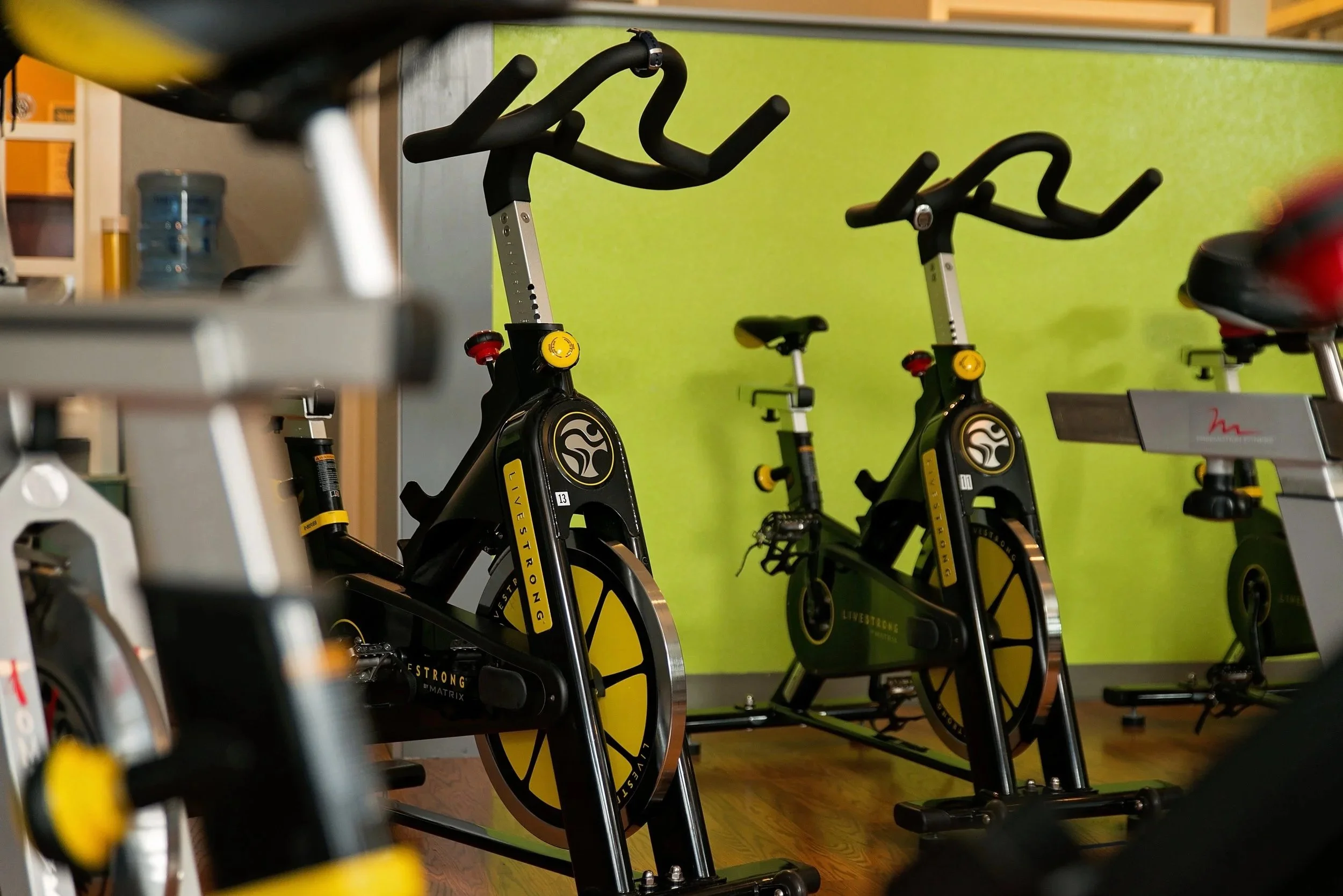 Multiple black and yellow stationary exercise bikes in a fitness studio with a light green wall