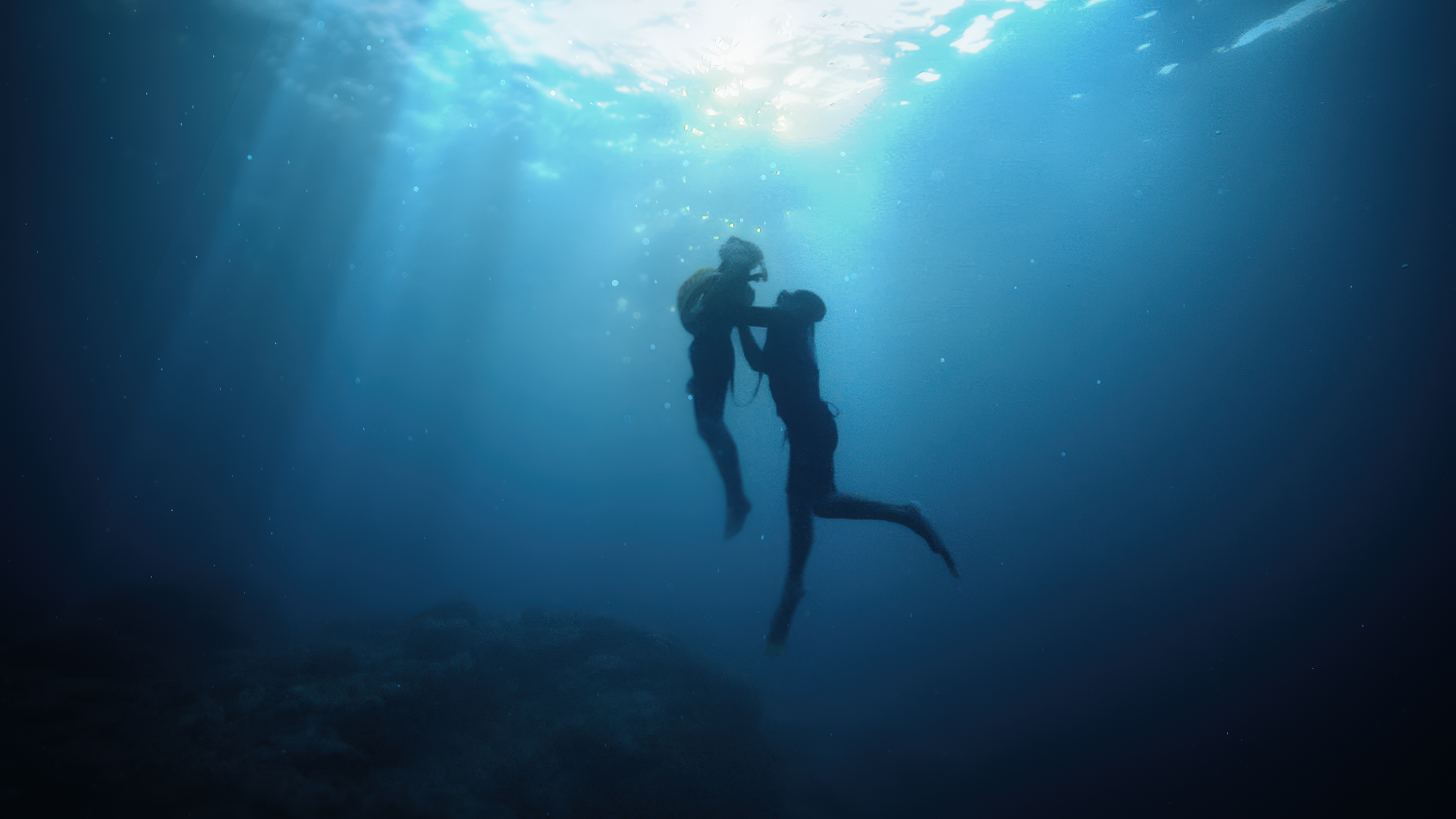 Two scuba divers underwater, holding hands, illuminated by sunlight from above.