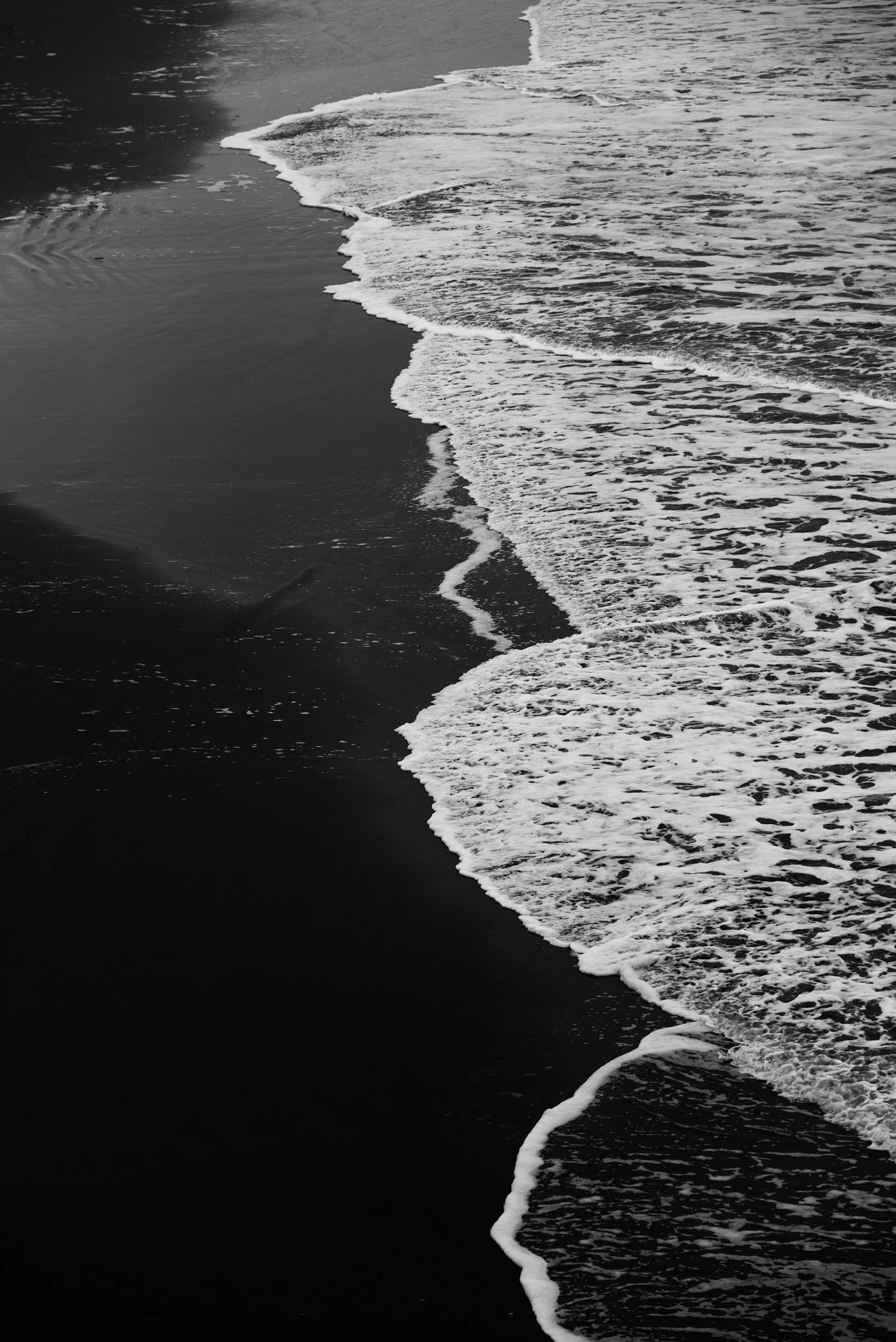 Black and white photograph of ocean waves washing onto a sandy beach.