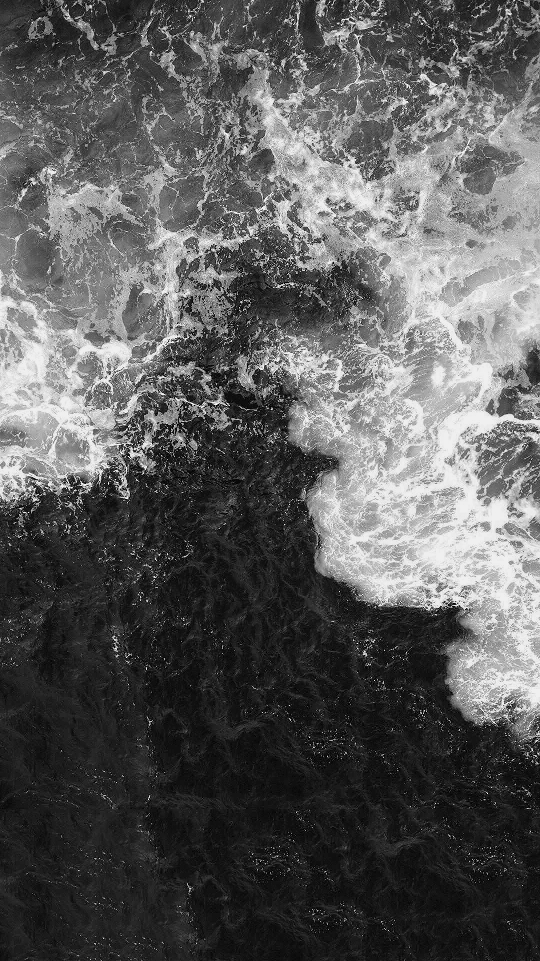 Black and white photo of sea waves crashing against rocky shoreline