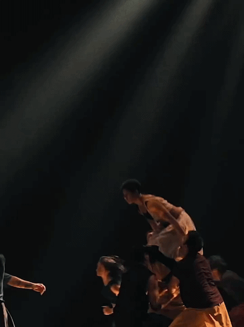 People in a dance or theatrical performance on a dark stage with dramatic lighting.