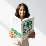 Woman smiling and reading a green-covered HR leadership book titled 'HR Leader 90 Day Playbook'