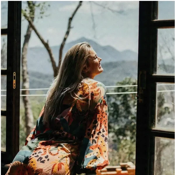 Woman smiling into the sun leaning out the window in a colorful dress after therapy with amy ros