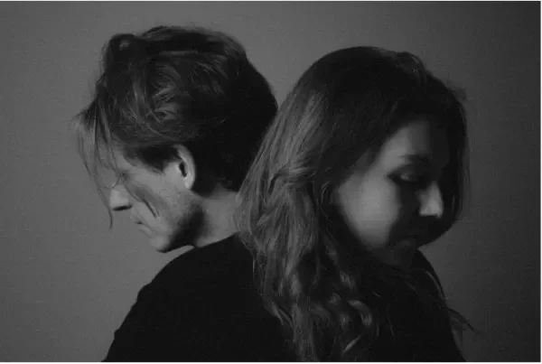 Black and white photo of woman and man backs to each other with heads tilted down
