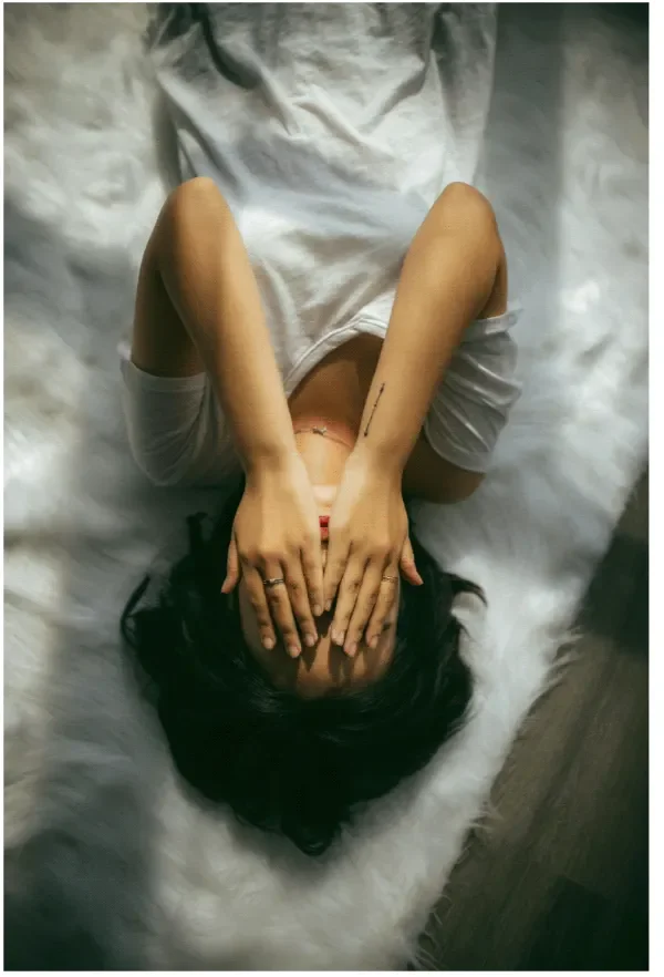 Woman covering her eyes in white t-shirt feeling overwhelmed