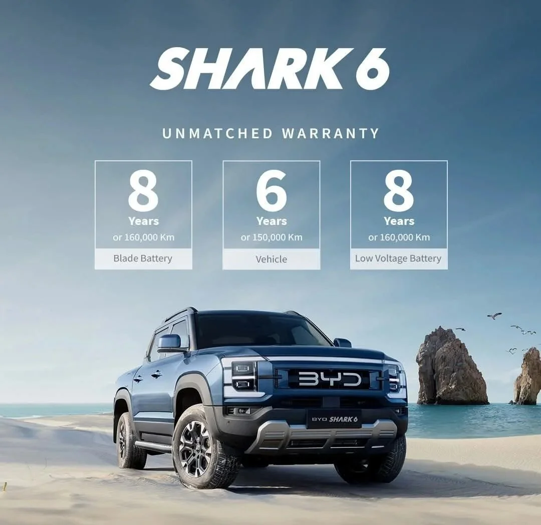 Advertisement for BYD Shark 6 vehicle, showing a blue electric truck on a beach with sea and rocks in background. Warranty details listed: 8 years for blade and low voltage batteries, 6 years for vehicle, with distances for each.