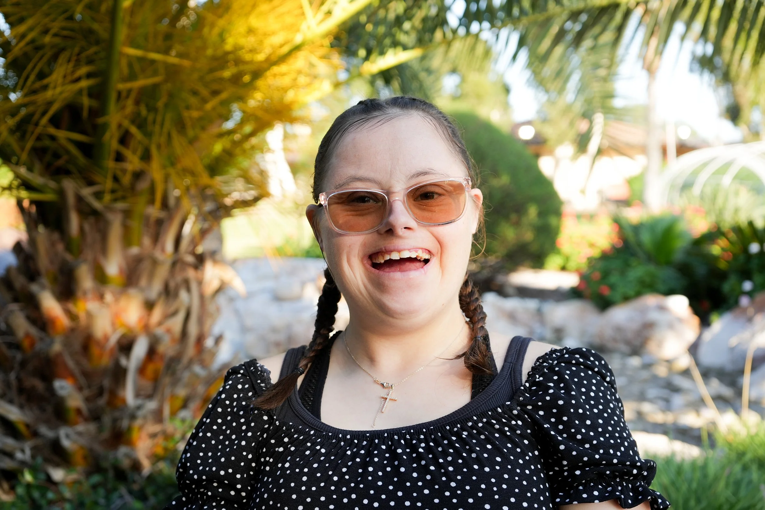 Woman with glasses smiles in front of greenery backdrop