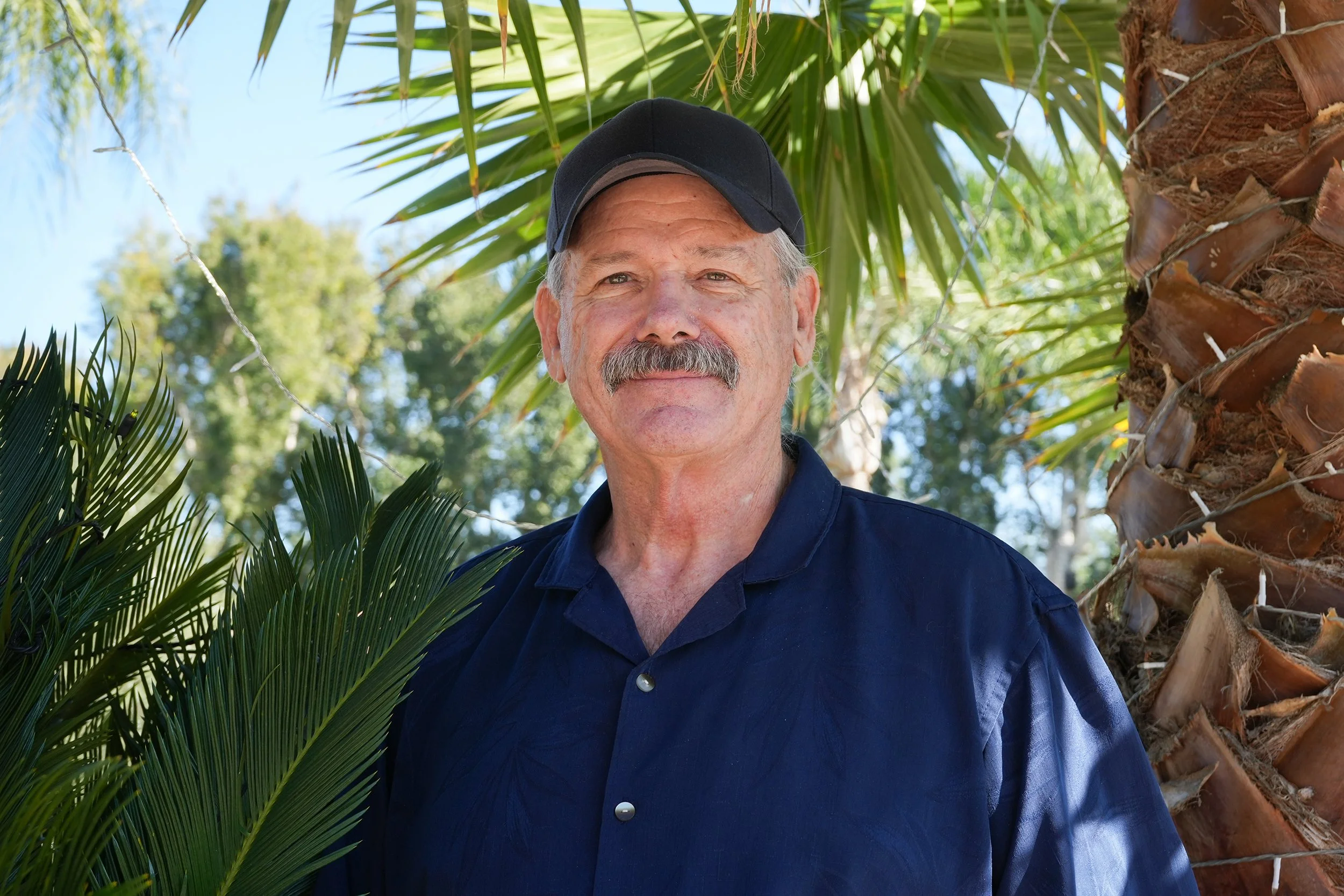 Headshot of man standing by palm trees