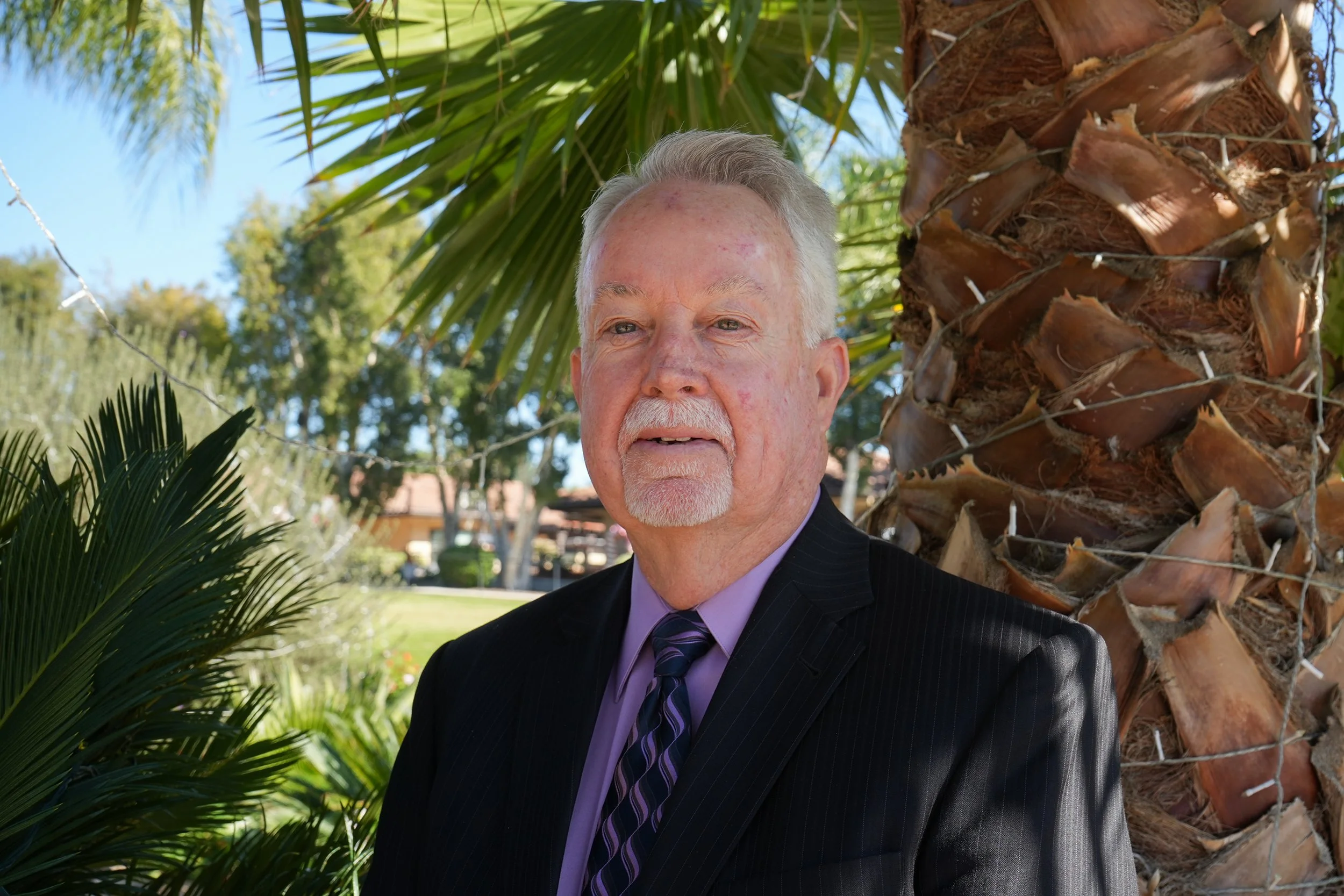 Headshot of man in suit and tie in front of palm trees