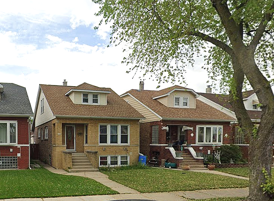 Two residential houses side by side with front yards and steps leading to the entrances, surrounded by trees on a partly cloudy day.