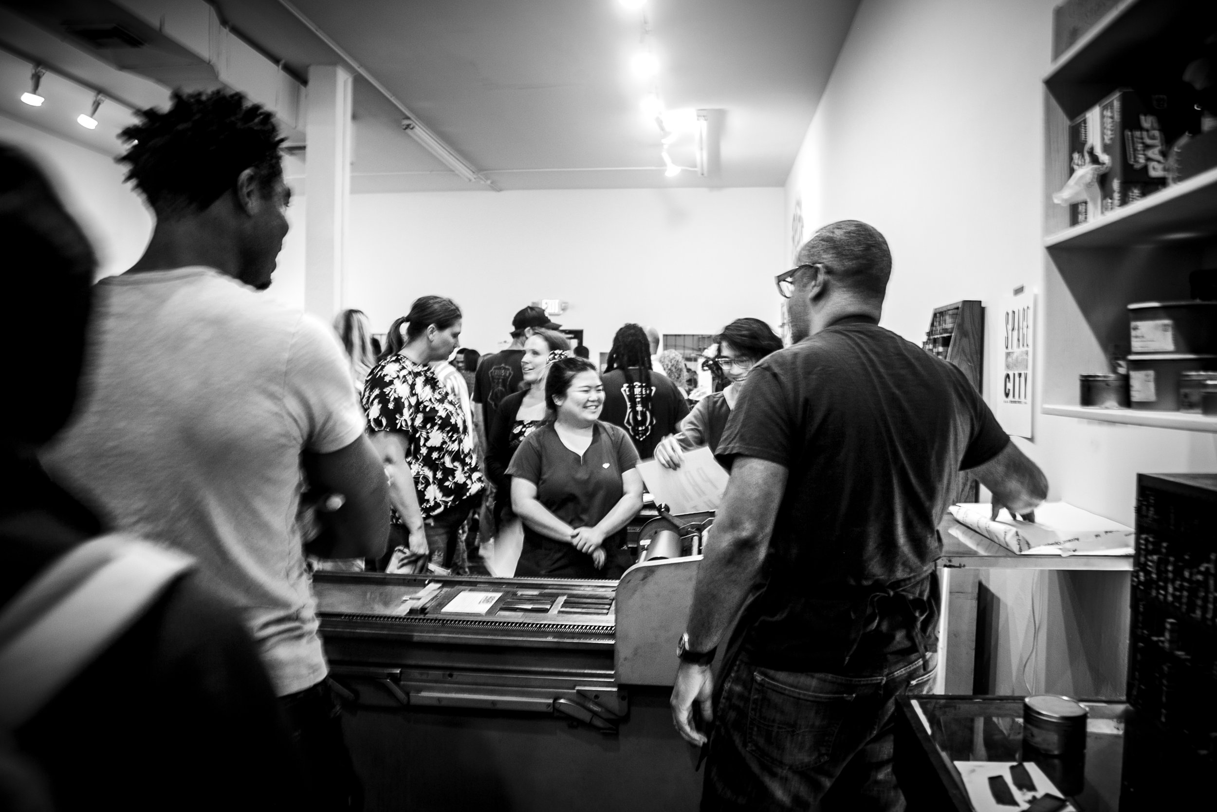 People gathered in line at a food or drink counter in a busy indoor setting, with some smiling and talking.