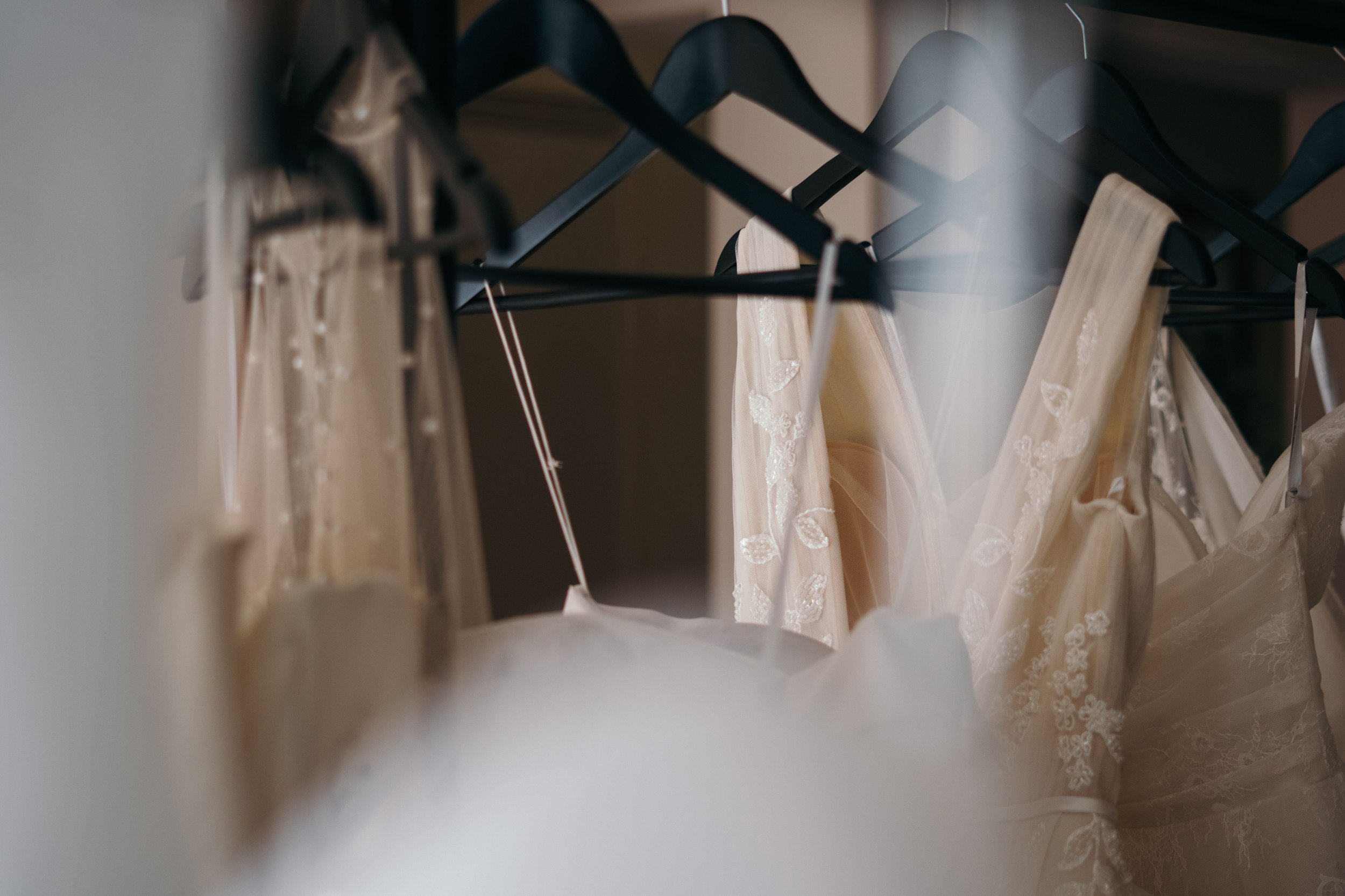 Hangers inside a closet holding several wedding dresses with lace details. Bridal Wardrobe Curation. Bridal Fashion