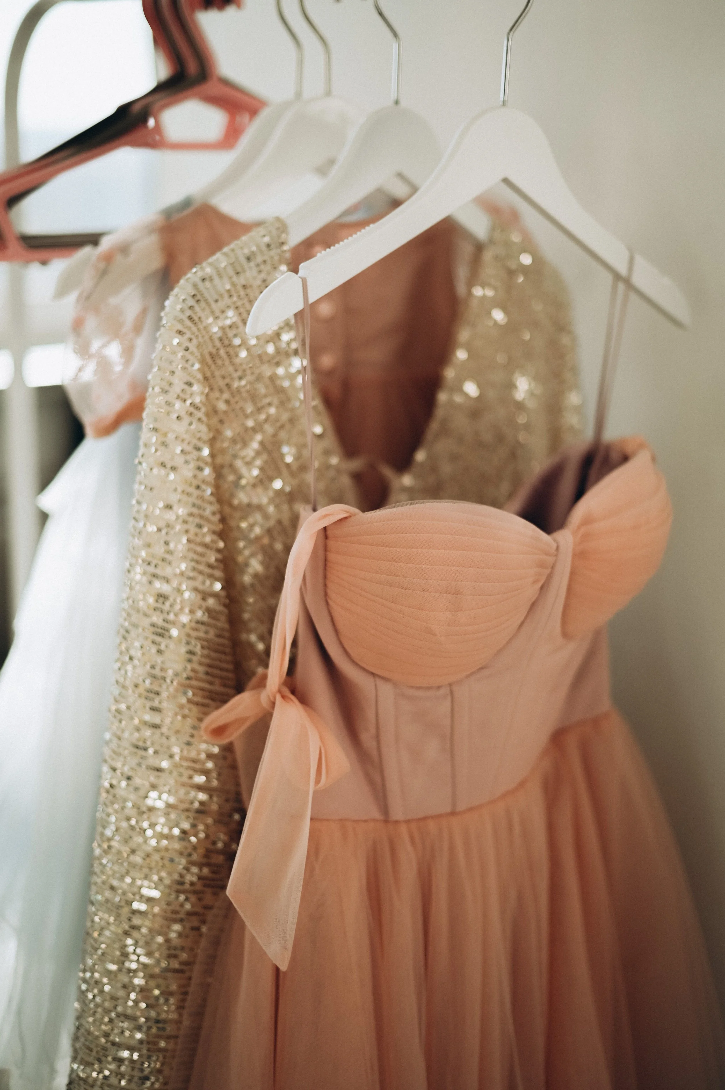 A collection of elegant dresses hanging on a clothing rack. The dresses are in soft, pastel colors with some adorned with sequins and embellishments. Bridal Wardrobe. Wedding Wardrobe. Bridal Fashion