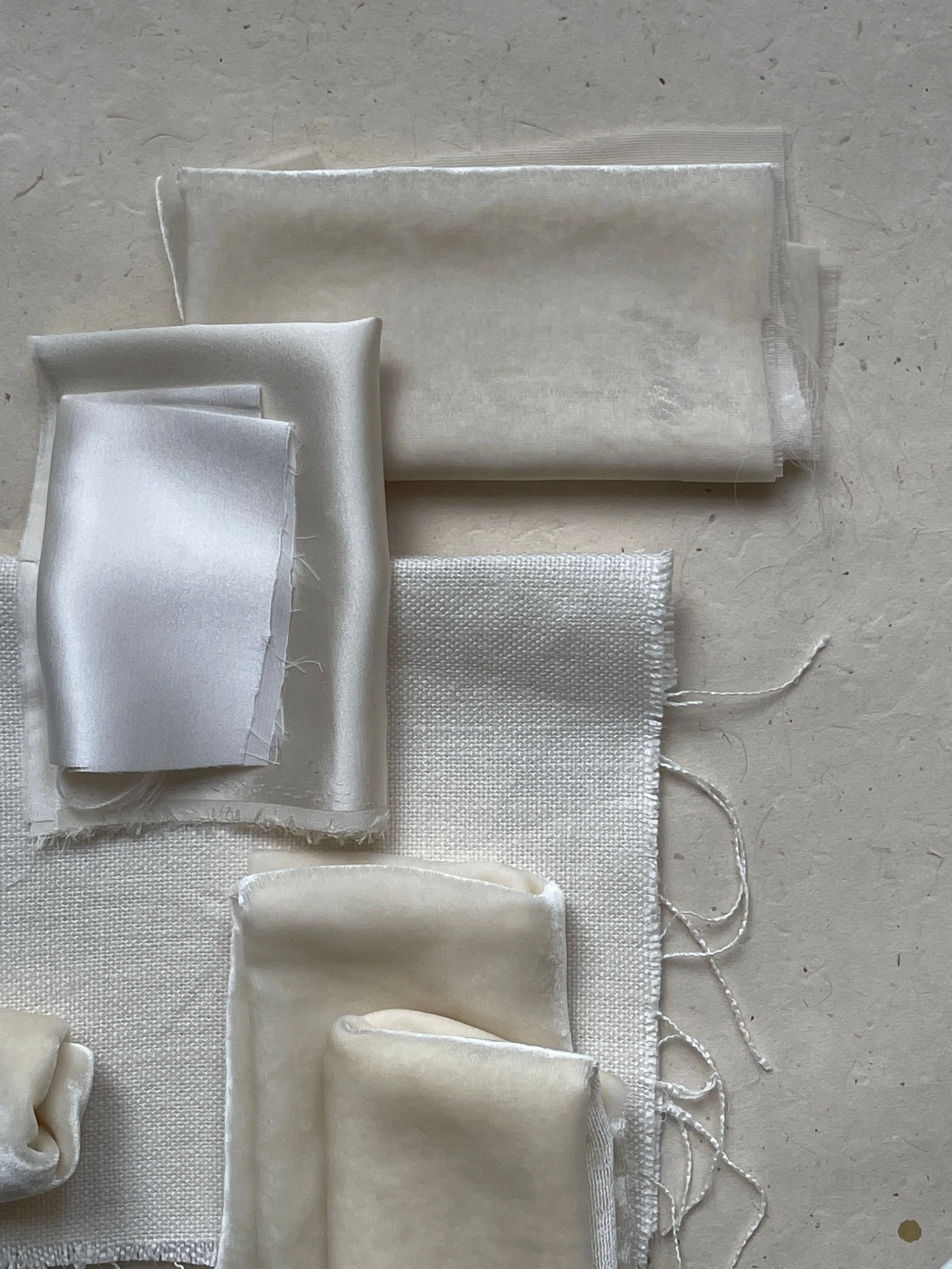 Various white fabric pieces and ribbons laid out on a light surface, including a small rolled-up fabric, a folded piece, and different textured strips.