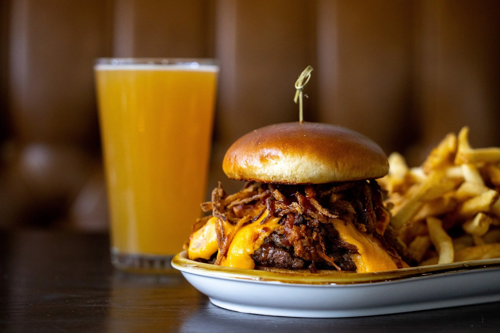 A plate with a cheeseburger topped with pulled pork and melted cheese, a side of French fries, and a glass of orange juice in the background.