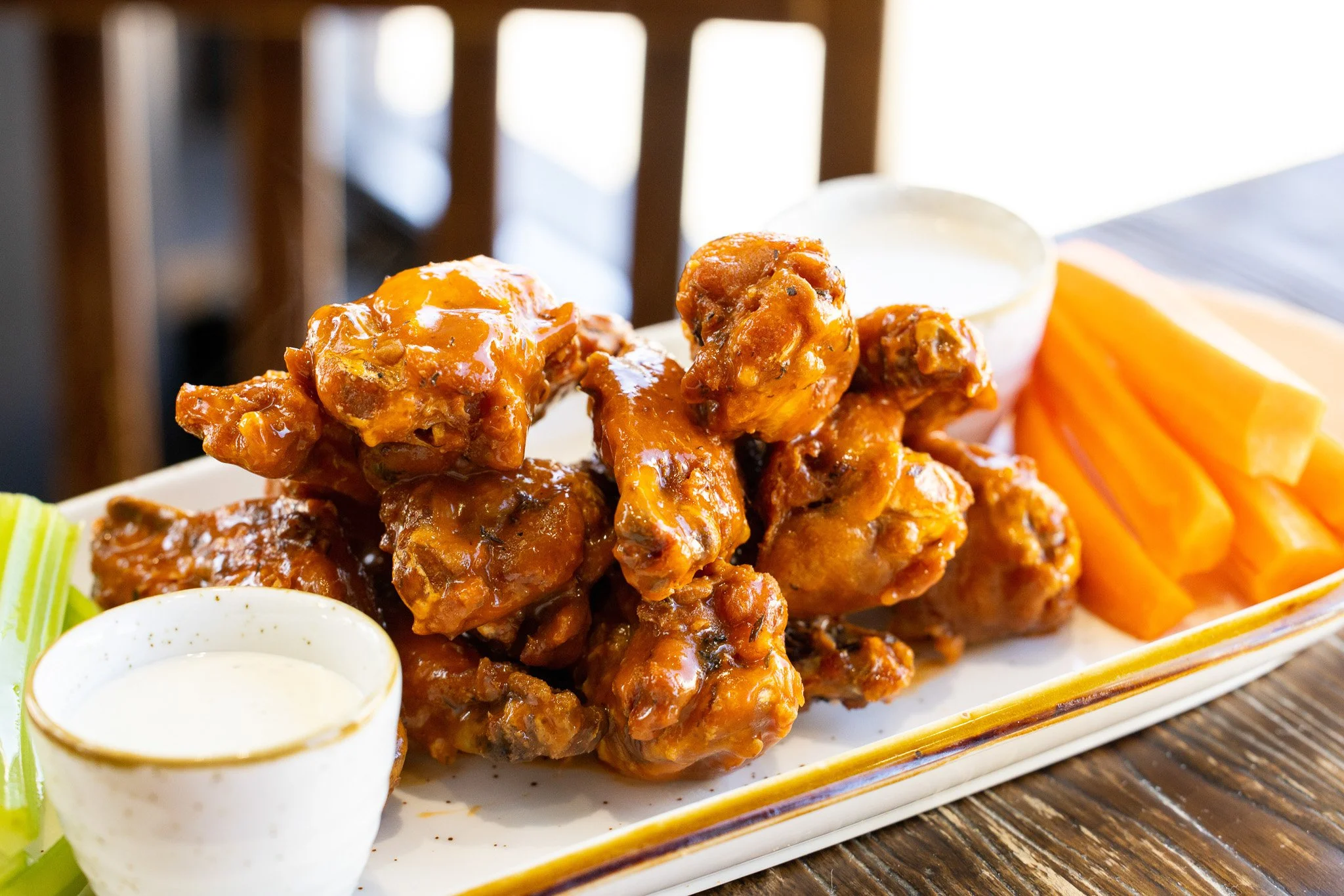 Buffalo chicken wings with blue cheese dressing and celery sticks on a white rectangular plate.
