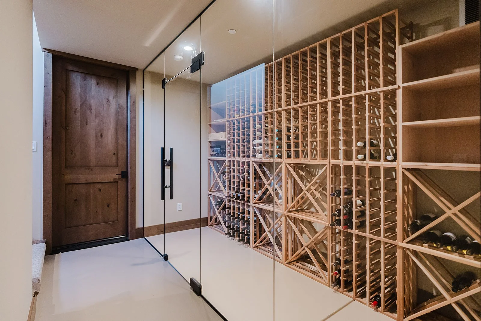 A wine cellar with a wooden door, glass door entrance, and wine racks filled with bottles.
