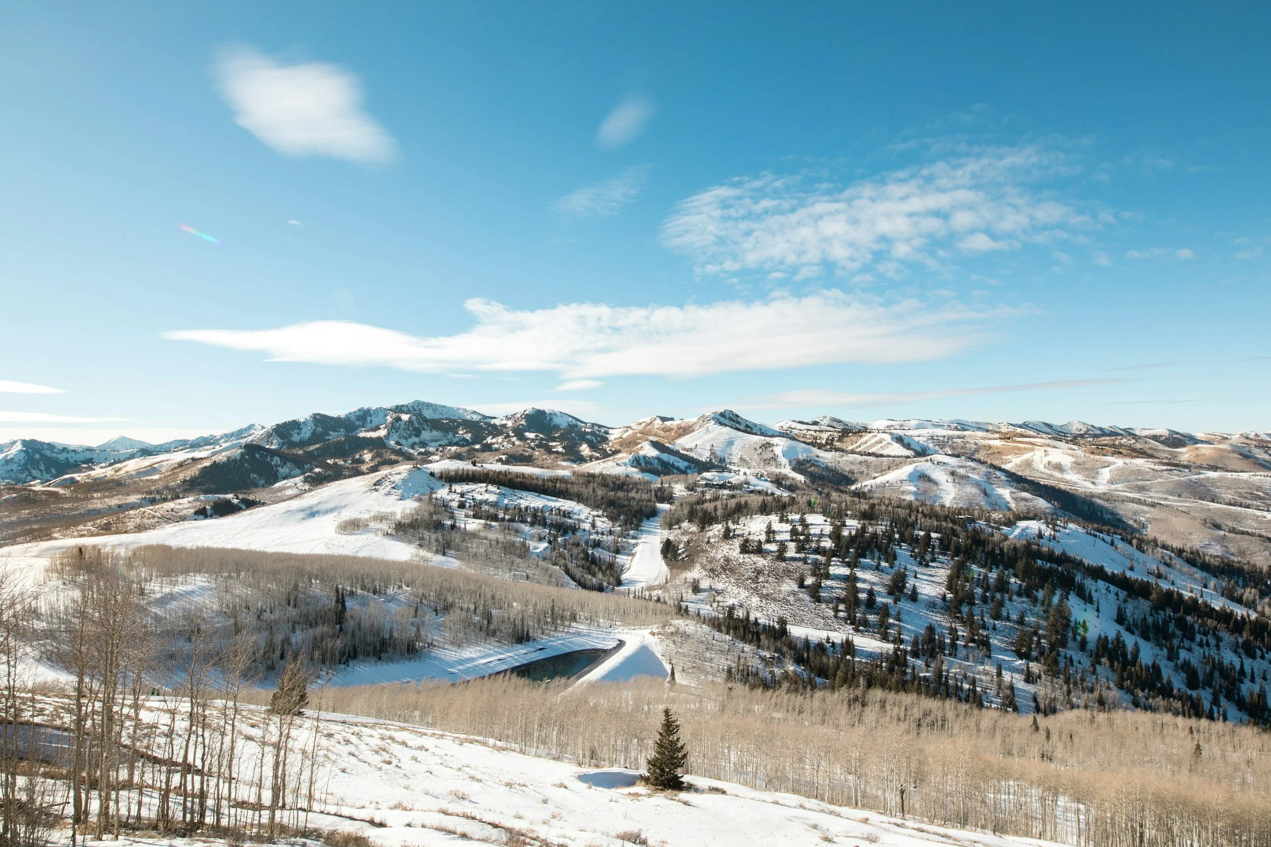 Snow-covered mountains and rolling hills under a partly cloudy sky with scattered clouds.