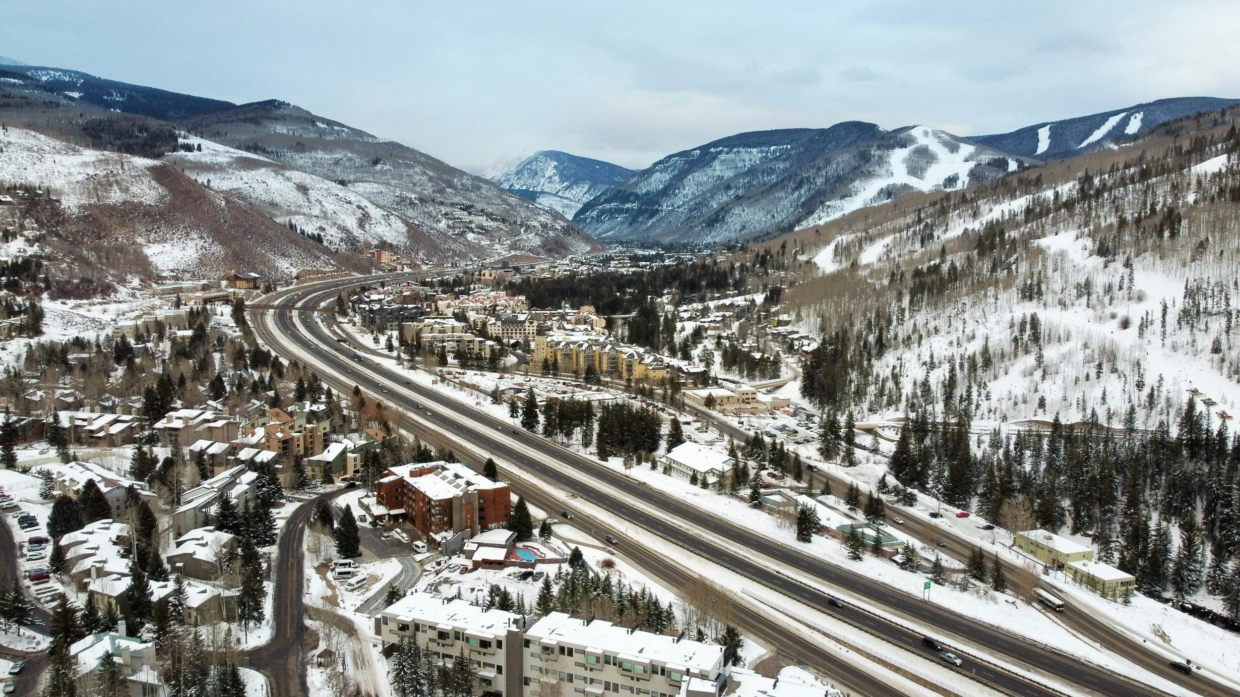 Snow-covered city in mountain valley with highway and residential buildings.