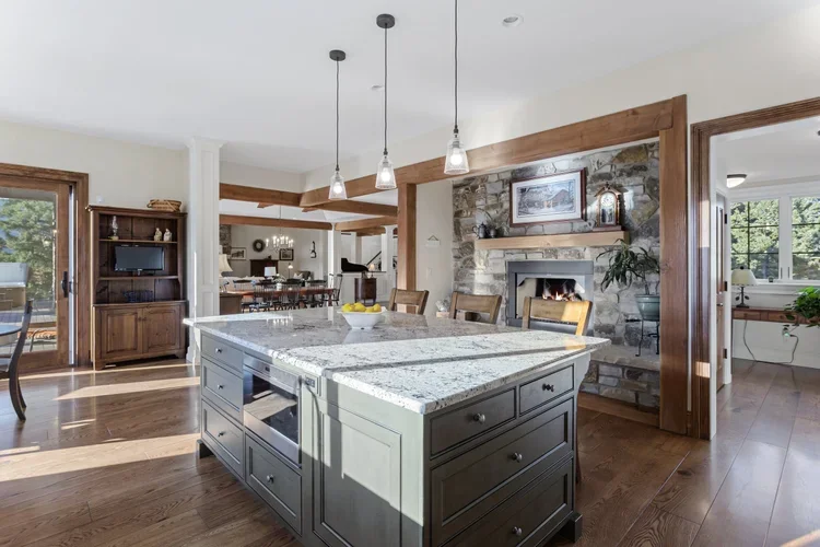 Open-concept kitchen and dining area with a large island, stone fireplace, and wooden accents.