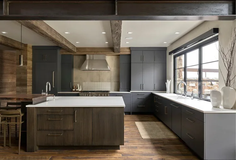 Modern kitchen with dark gray cabinets, white countertops, wood accents, and large window with a view outside.
