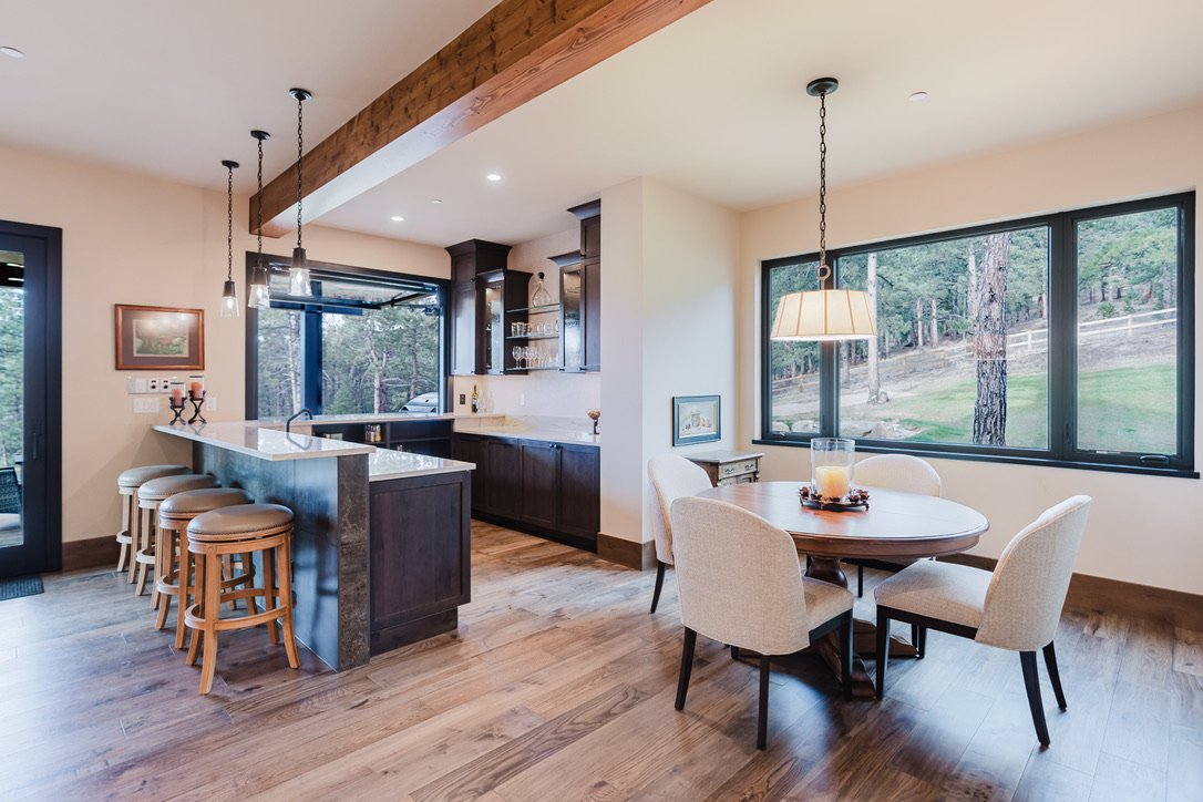 Open-concept kitchen and dining area with large window overlooking trees, dark wooden cabinetry, and a round dining table with four chairs.